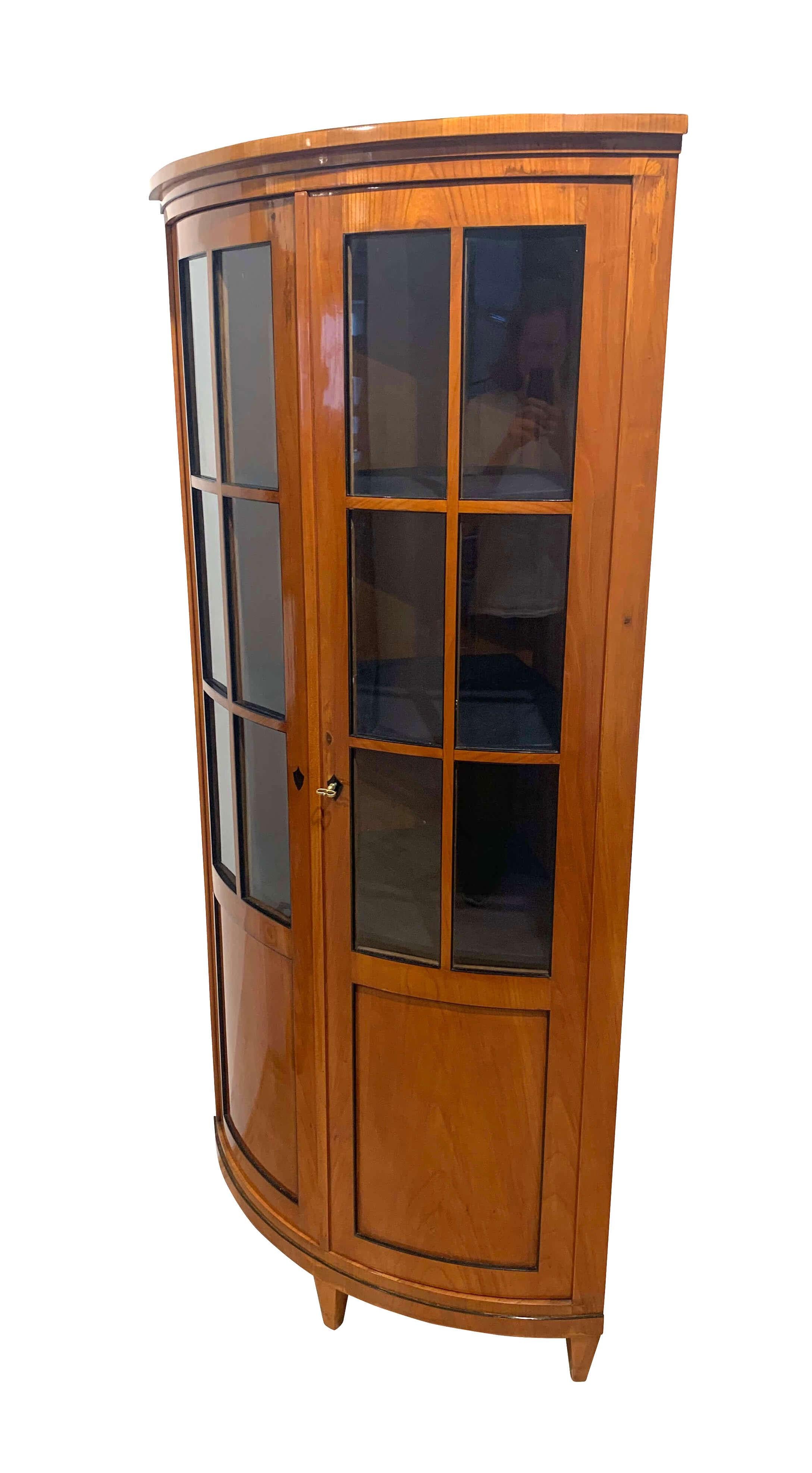 Lovely neoclassical corner showcase or vitrine from the second Biedermeier period, circa 1880.

Wood: Cherry veneer and solid wood, shellac hand-polished. Partly ebonized (inner) edges. Two lockable doors with six windows each. Coat of arms inlaid