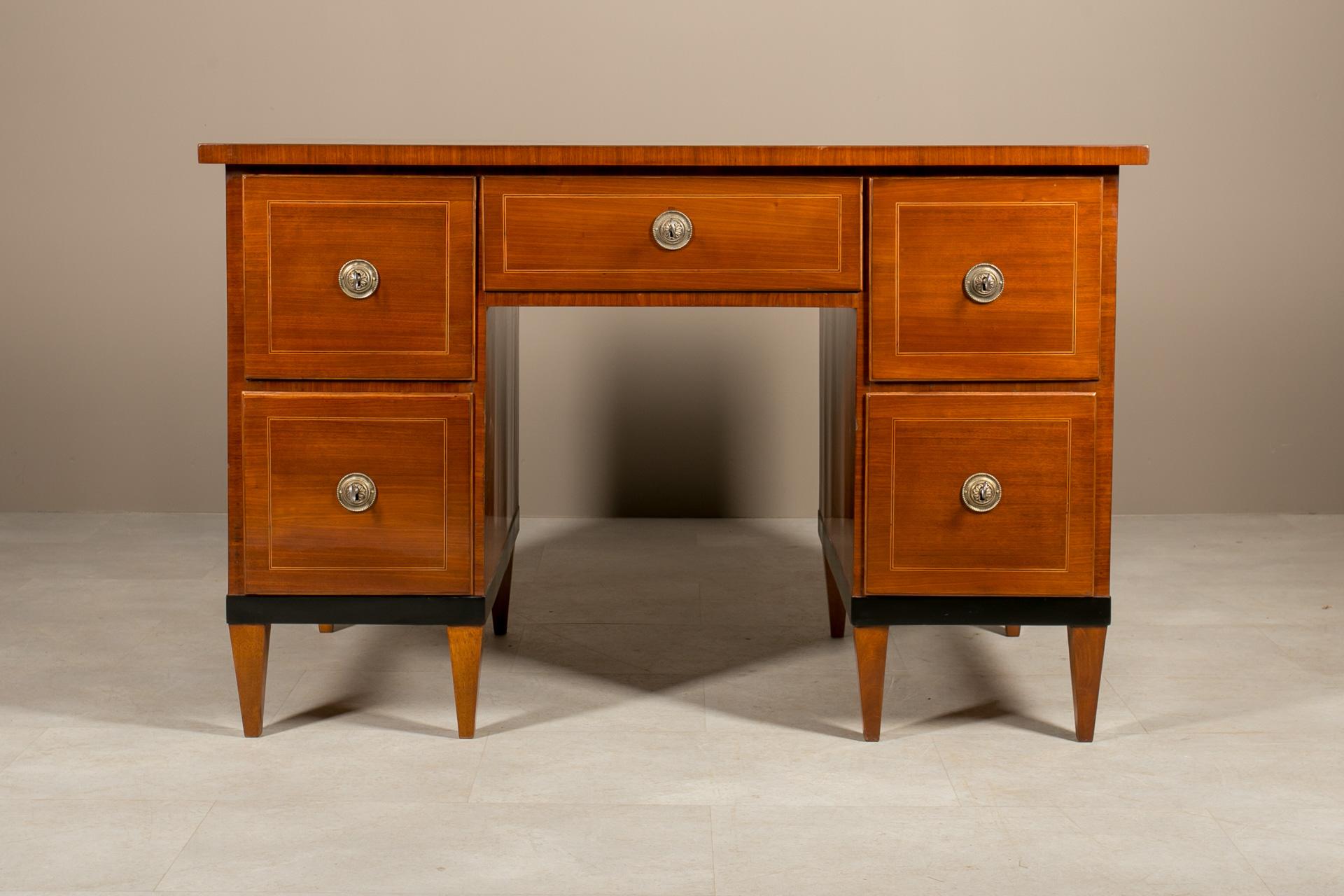 Se trata de un precioso escritorio de cinco cajones del periodo Biedermeier. Se fabricó en Alemania hacia la década de 1830. La pieza está chapada en madera de nogal con una extraordinaria incrustación de vetas de roble negro y arce en los cajones,
