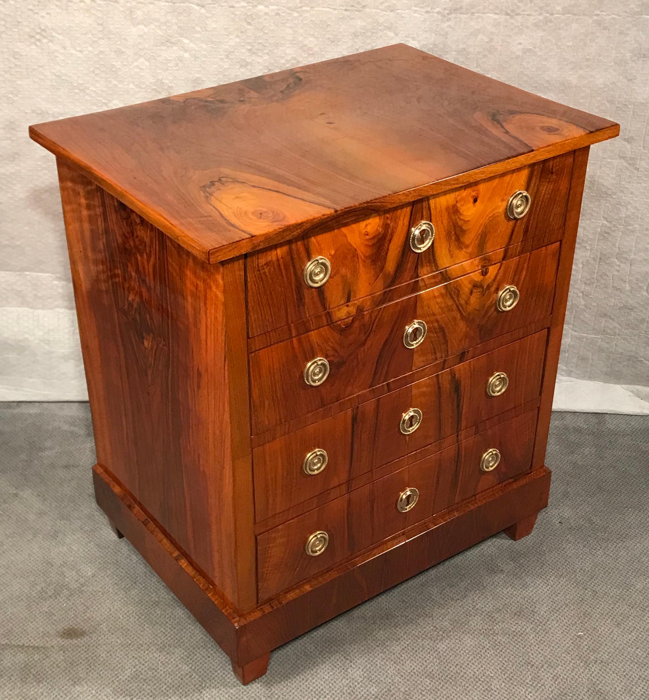 This small Biedermeier dresser dates back to around 1830. The four drawer commode has a very pretty walnut veneer on top, sides and front. 
It has been professionally refinished with a shellac polish. The straight lines of this piece and the