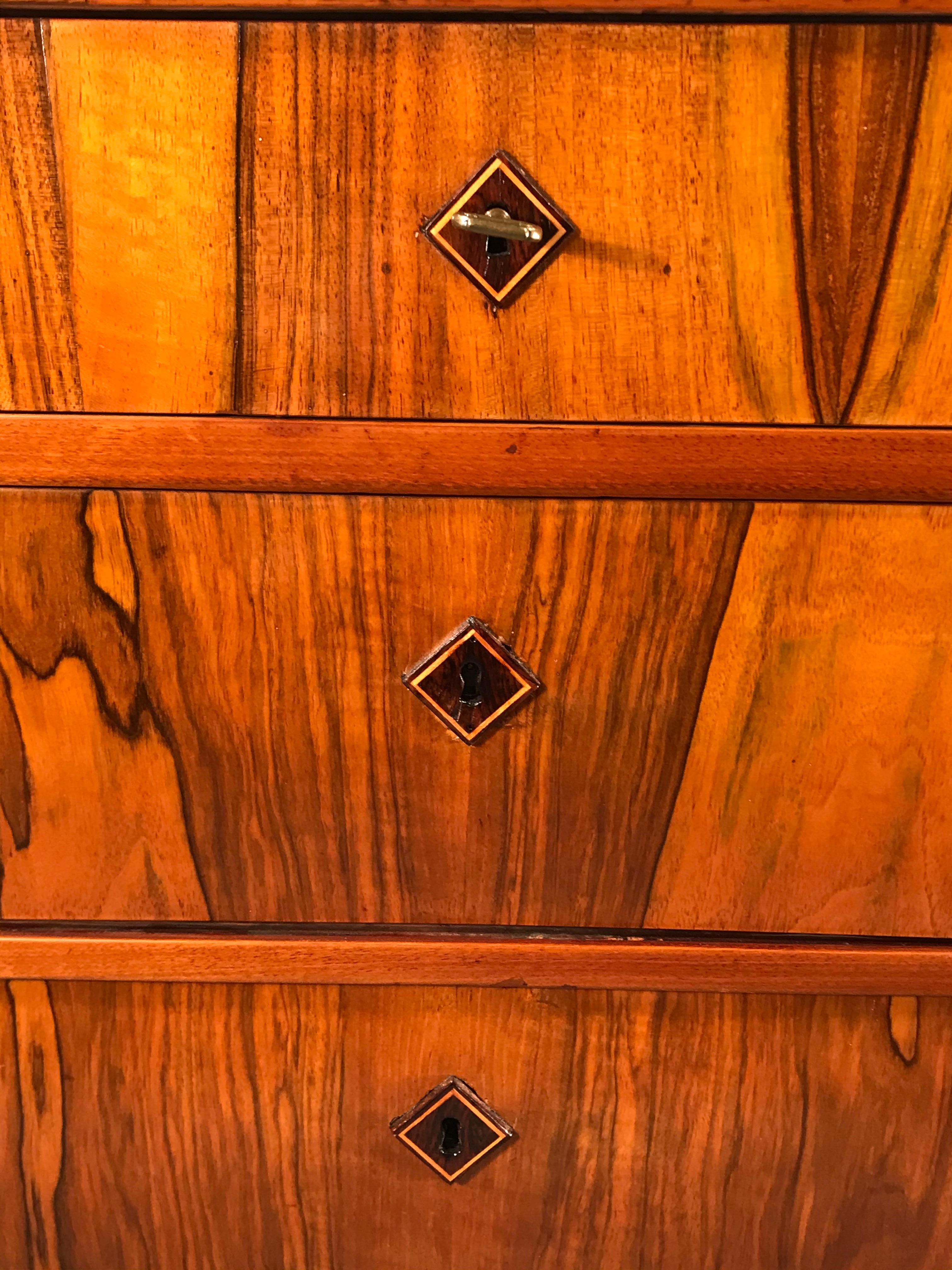 This beautiful three-drawer 1820s Biedermeier dresser’s organic vibrant walnut veneer grain and the sleek design makes this piece the perfect addition for any interior style. The charming wooden escutcheons are original. The chest of drawers is in