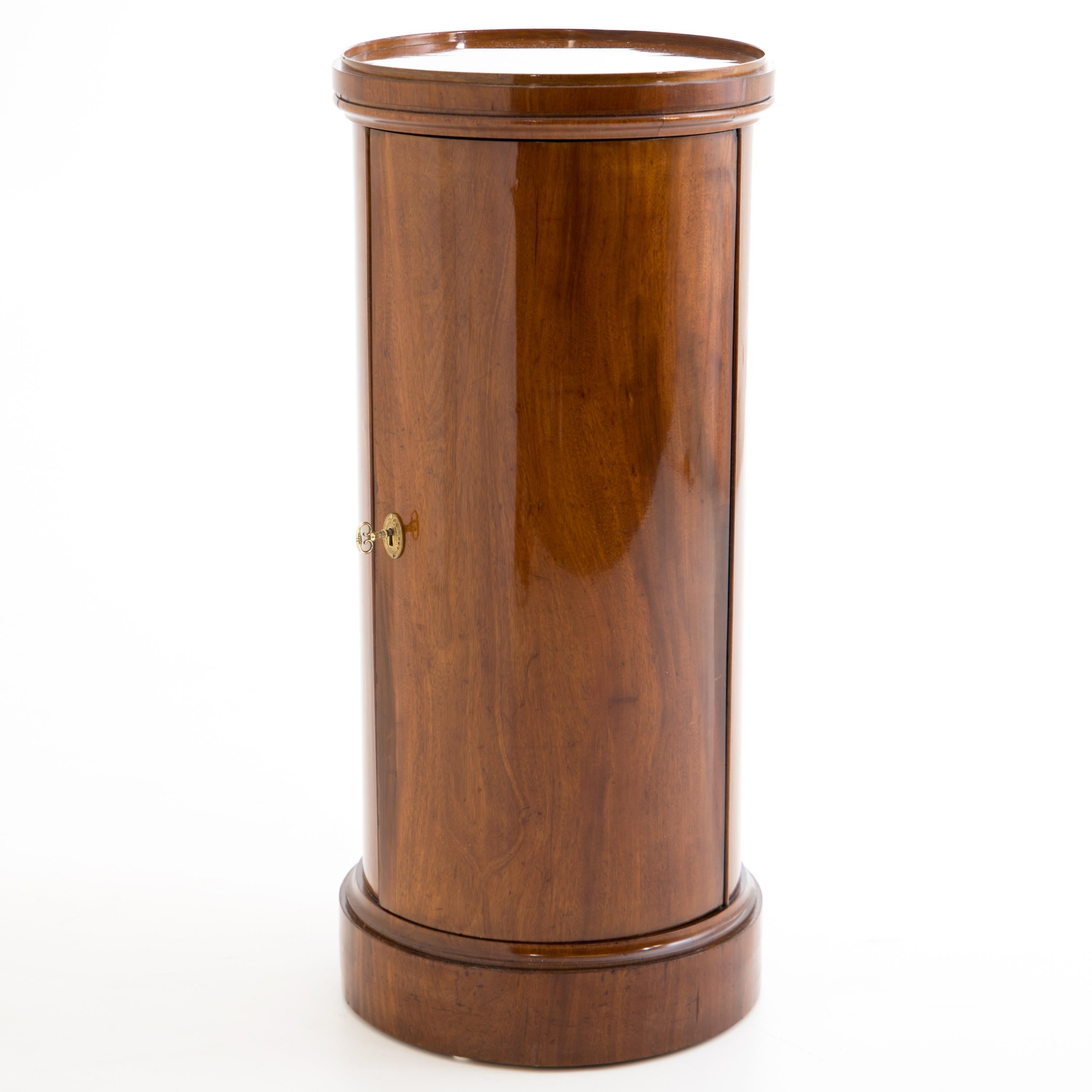 Biedermeier Drum cabinet veneered in mahogany. The round body with one door stands on a slightly profiled plinth. The top is also slightly profiled and veneered. The interior division consists of two shelves. The cabinet has been expertly restored