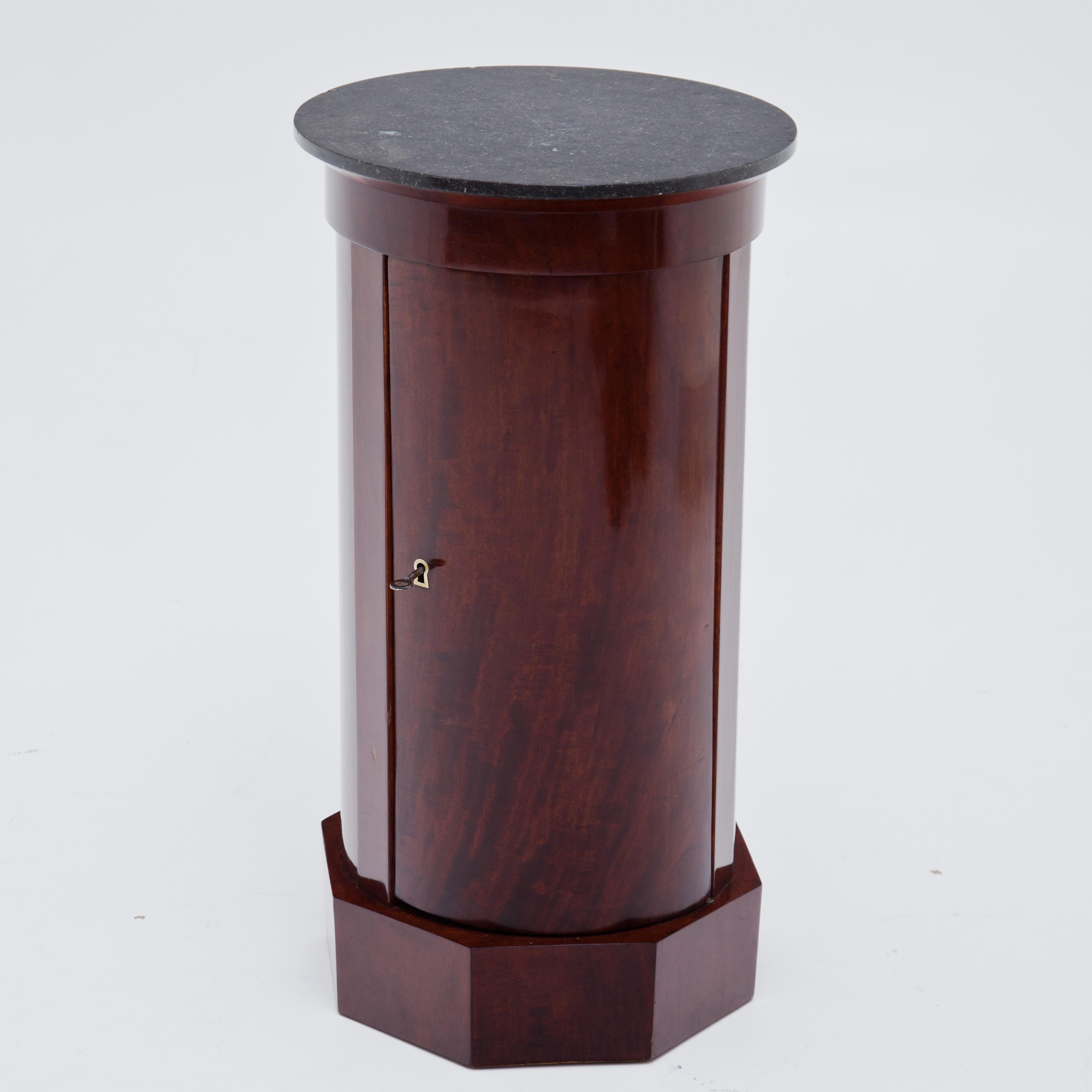 Biedermeier drum cabinet on octagonal base with round body and black marble top. Inside two shelves. Mahogany veneer.