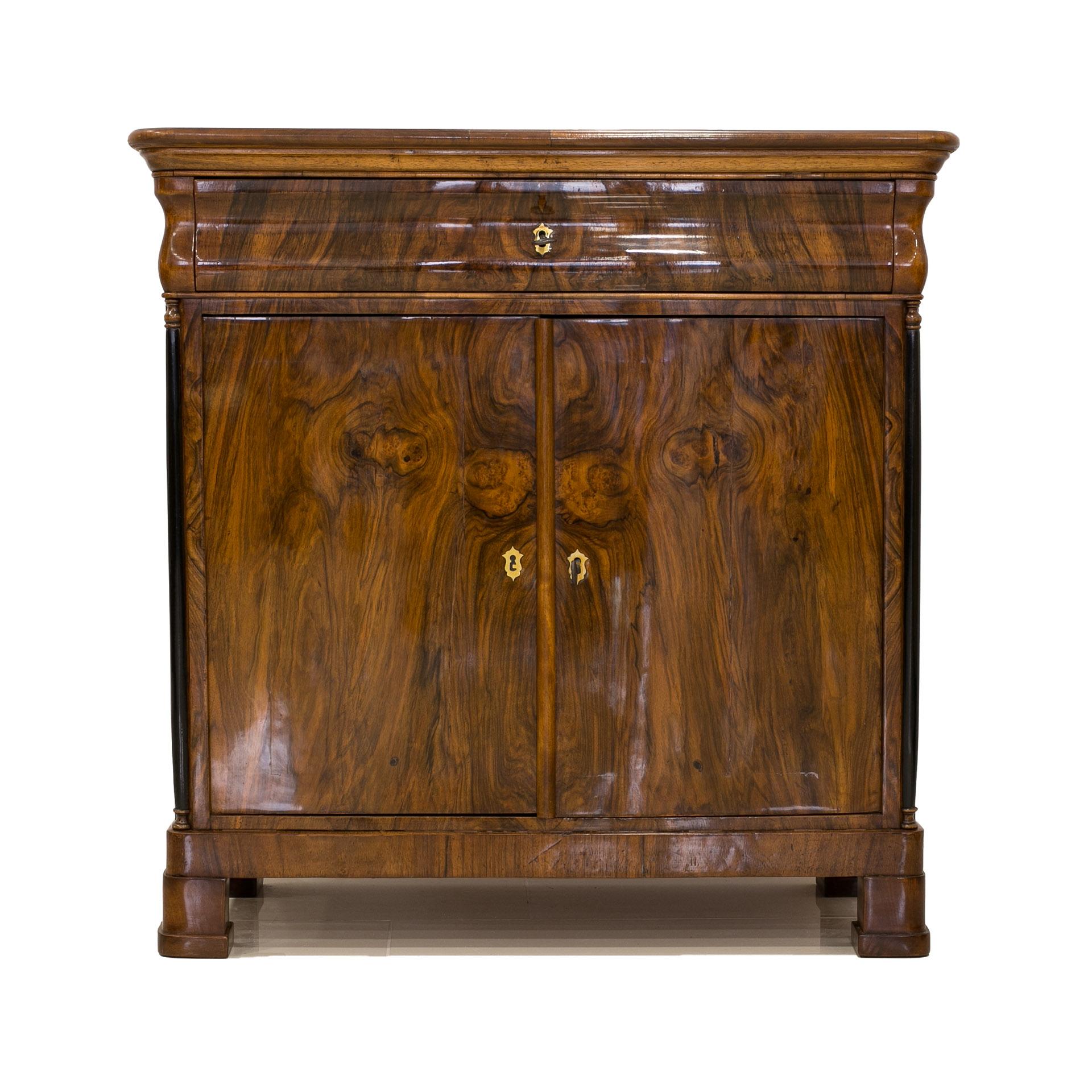 This Biedermeier-era commode was made in Germany in the first half of the 19th century. The furniture is made of coniferous wood, veneered with walnut veneer that presents beautiful wood patterns. It features one practical drawer in the top section