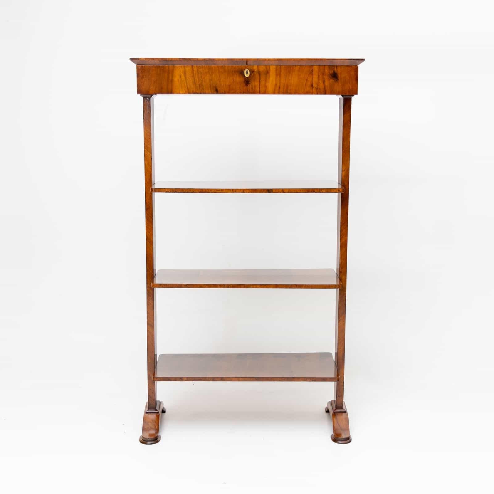 Biedermeier bookshelf with three shelves and a lockable hinged compartment. The étagère is veneered with walnut and stands on slightly curved feet.