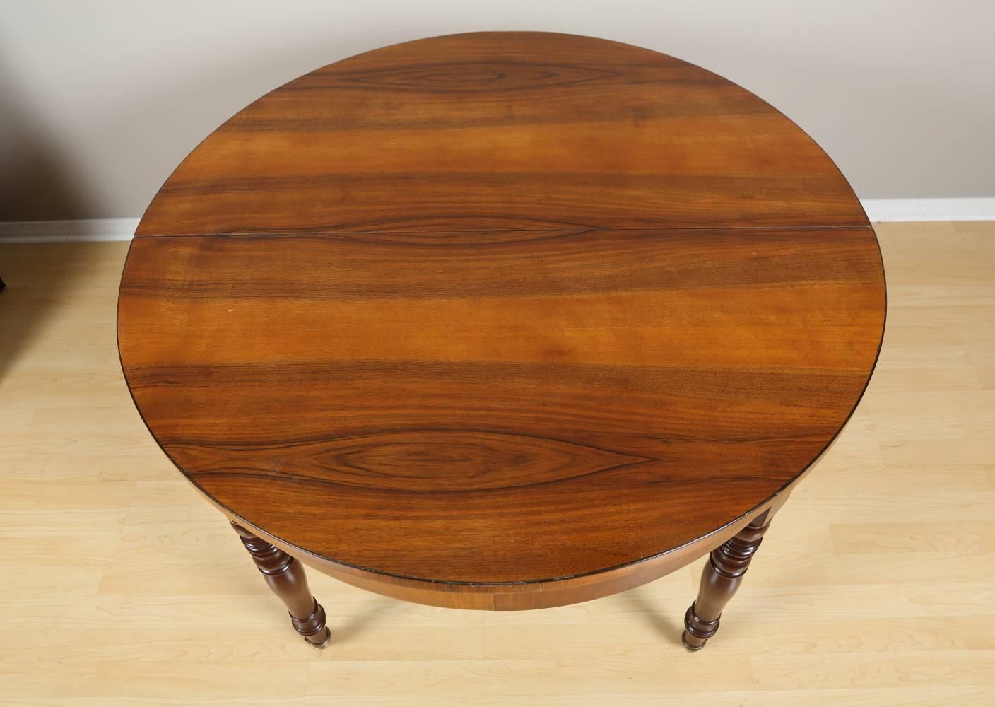 Biedermeier extending dining table, circa 1850 from Germany. This spectacular walnut dining table features beautifully veneered top resting on elegantly rounded legs finished off with small casters. The table includes four leafs at 19.5