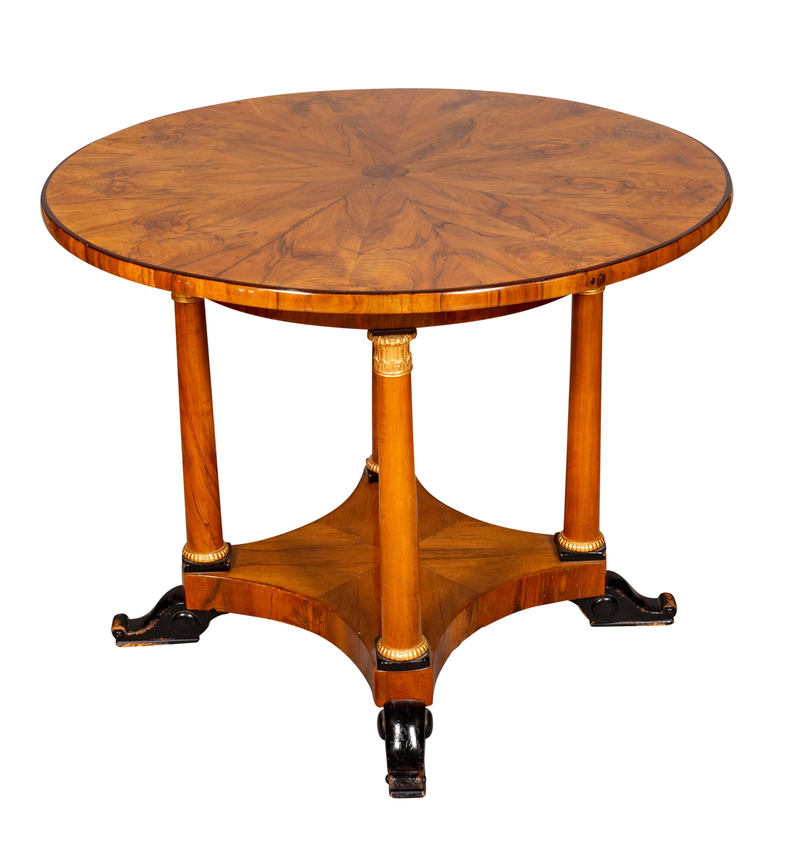 Circular top with kaleidoscope sunburst top with book matched veneers raised on four cylindrical legs with gilded capitols, conforming plinth base with ebonized feet.