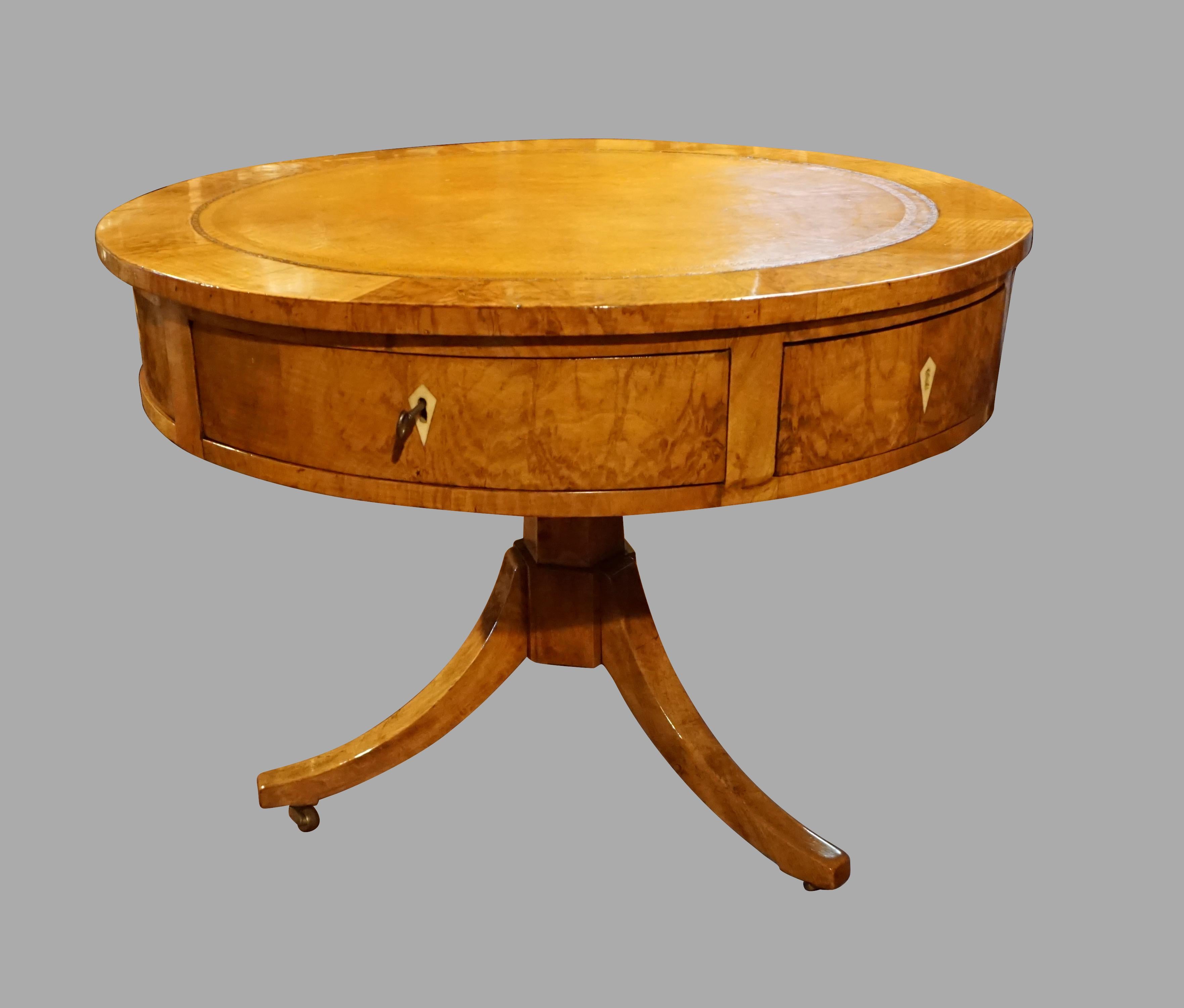 A handsome fruitwood Continental Biedermeier center table, the rotating tan gilt-tooled leather top above 2 rectangular drawers and 5 wedge shaped drawers, supported on a hexagonal tripod base ending in brass casters. Probably Austrian or Northern