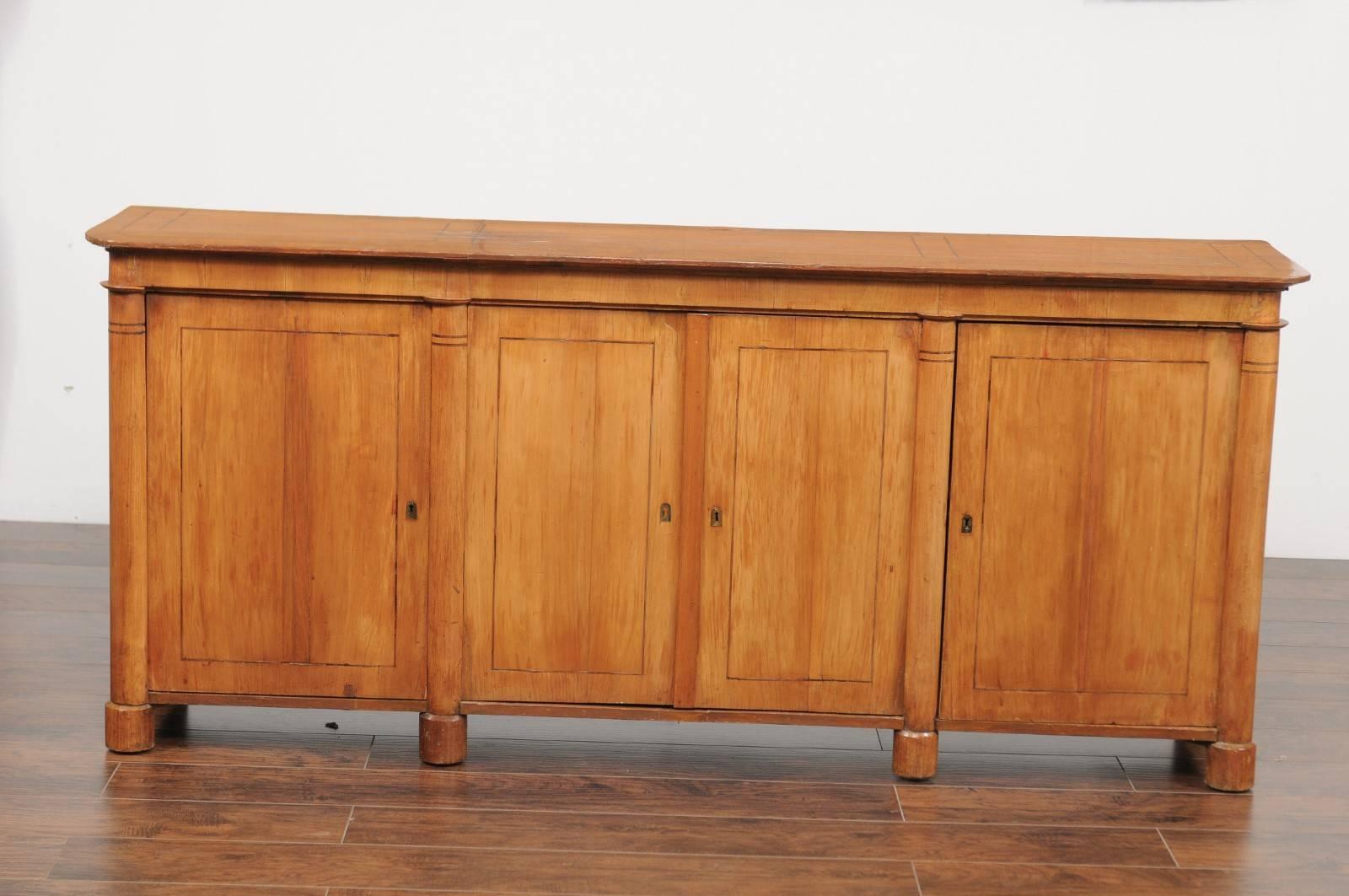 A German Biedermeier fruitwood veneered four-door enfilade with Doric-style semi-columns from the mid-19th century. This Biedermeier long buffet features a rectangular top with rounded corners and thin banded inlay, surmounting a set of double doors