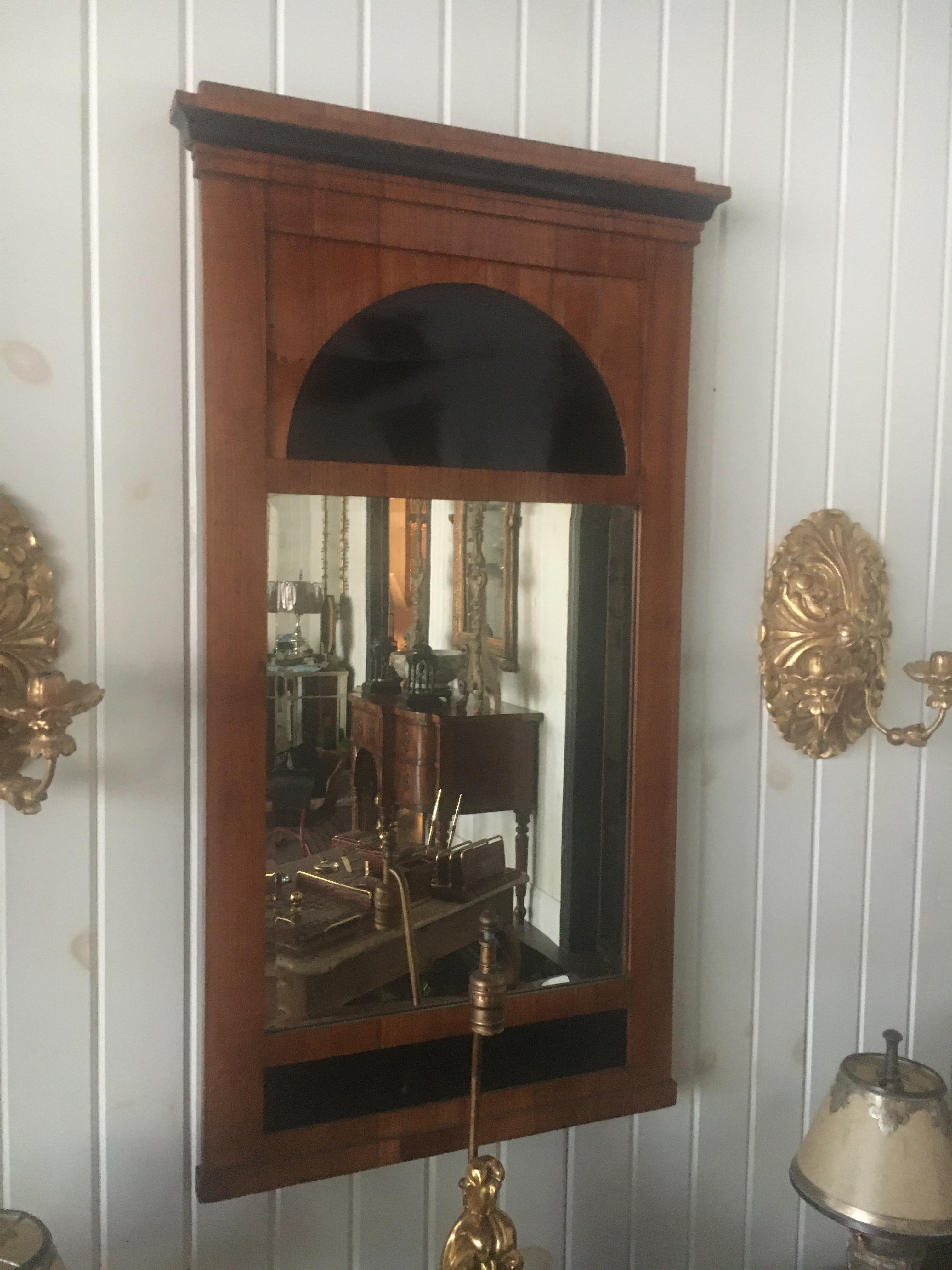 Specchio da molo Biedermeier in legno di frutta 
xIX secolo 
con una cornice sporgente modanata sopra un pannello intagliato per mostrare una demilune e una lastra di specchio verticale rettangolare smussata. 
Misura: altezza 41 x larghezza 22