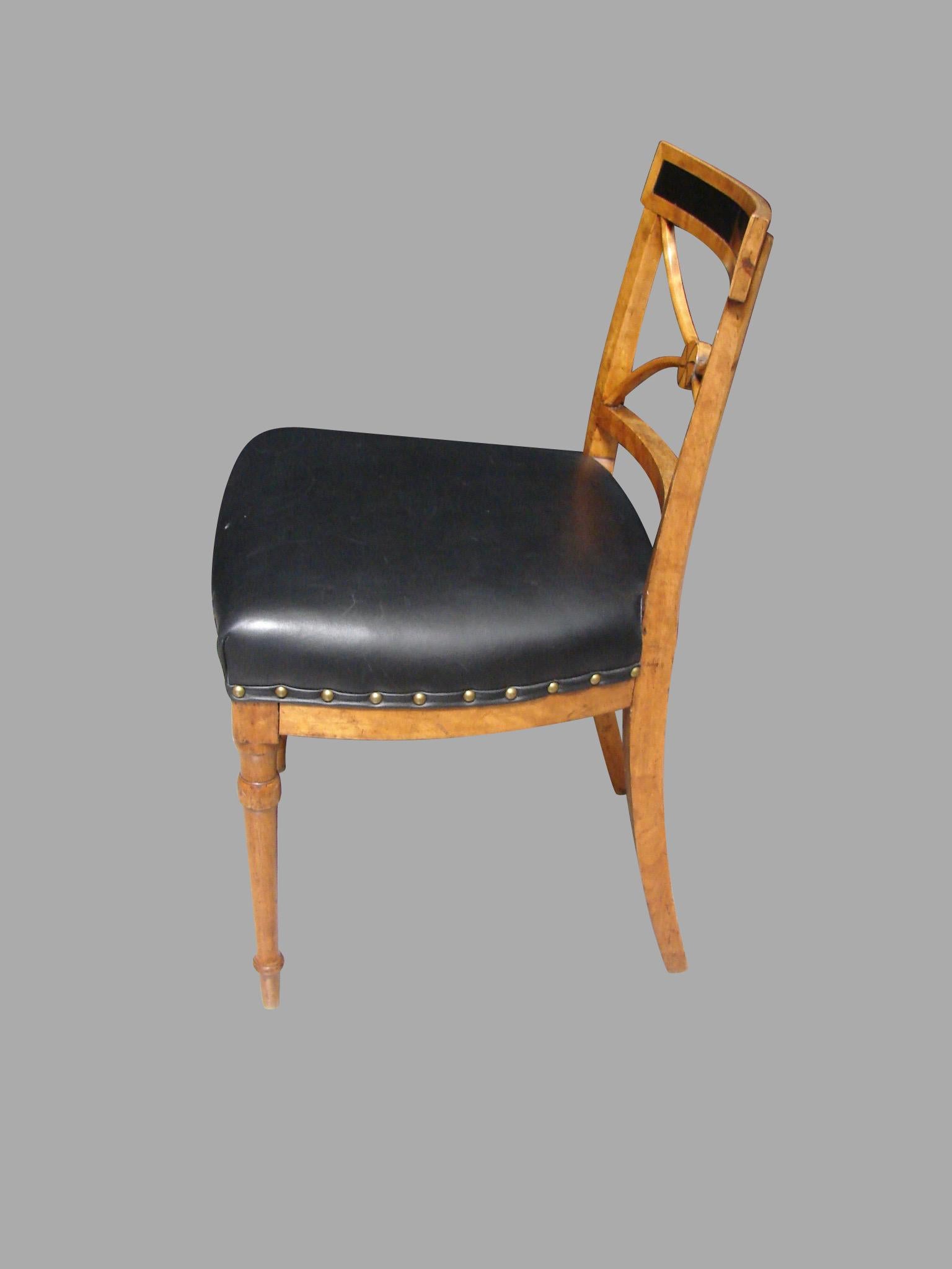 A pretty Biedermeier satin birch side chair, the back with an ebonized top rail above a stylized splat centered with a boss, the seat upholstered in black leather, all supported on turned legs, circa 1820.