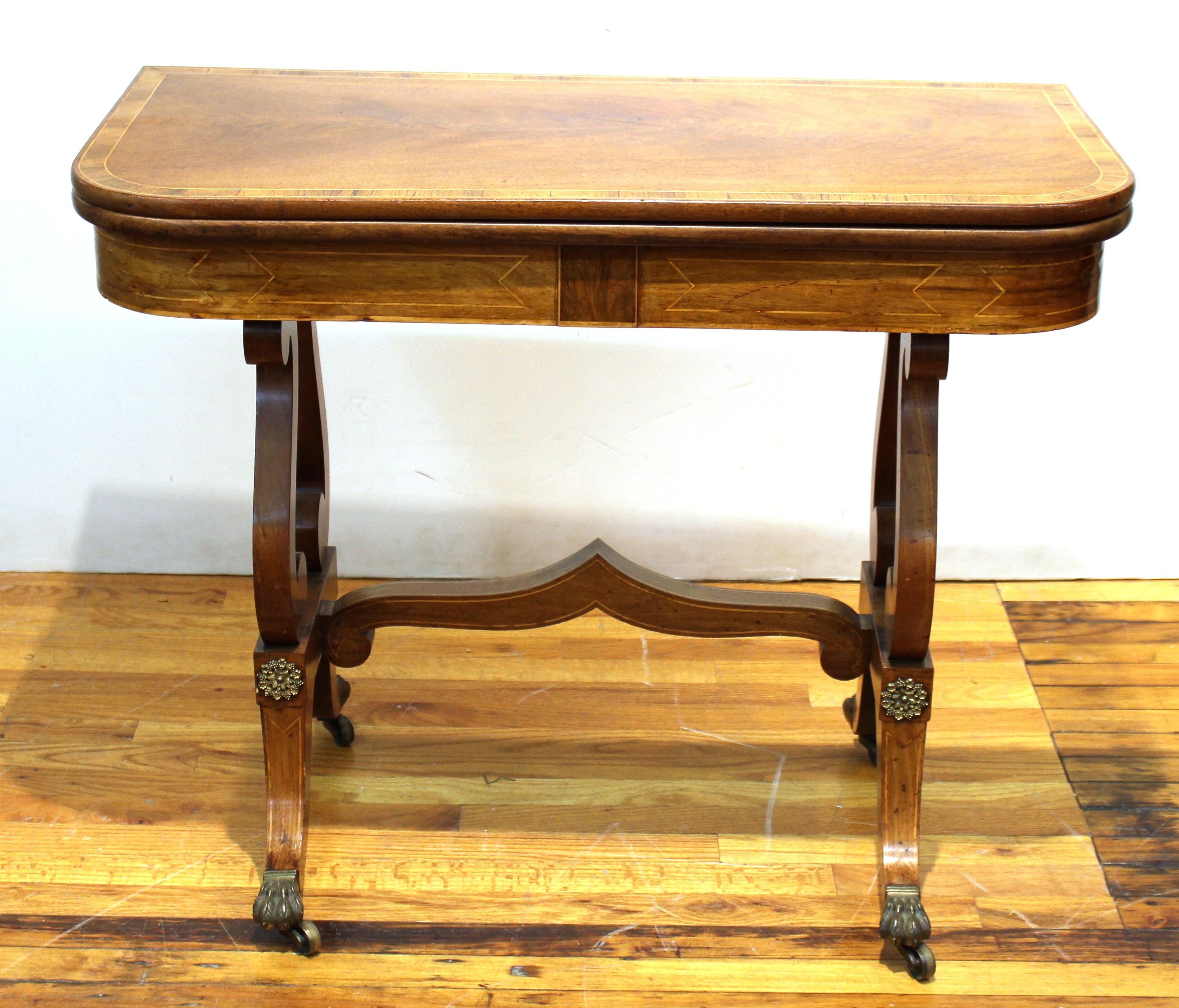 Biedermeier games table in blonde burl with a mahogany veneered lyre base atop scroll feet with metal embellishments and a flip top. The piece dates from the early 19th century and is in great antique shape.