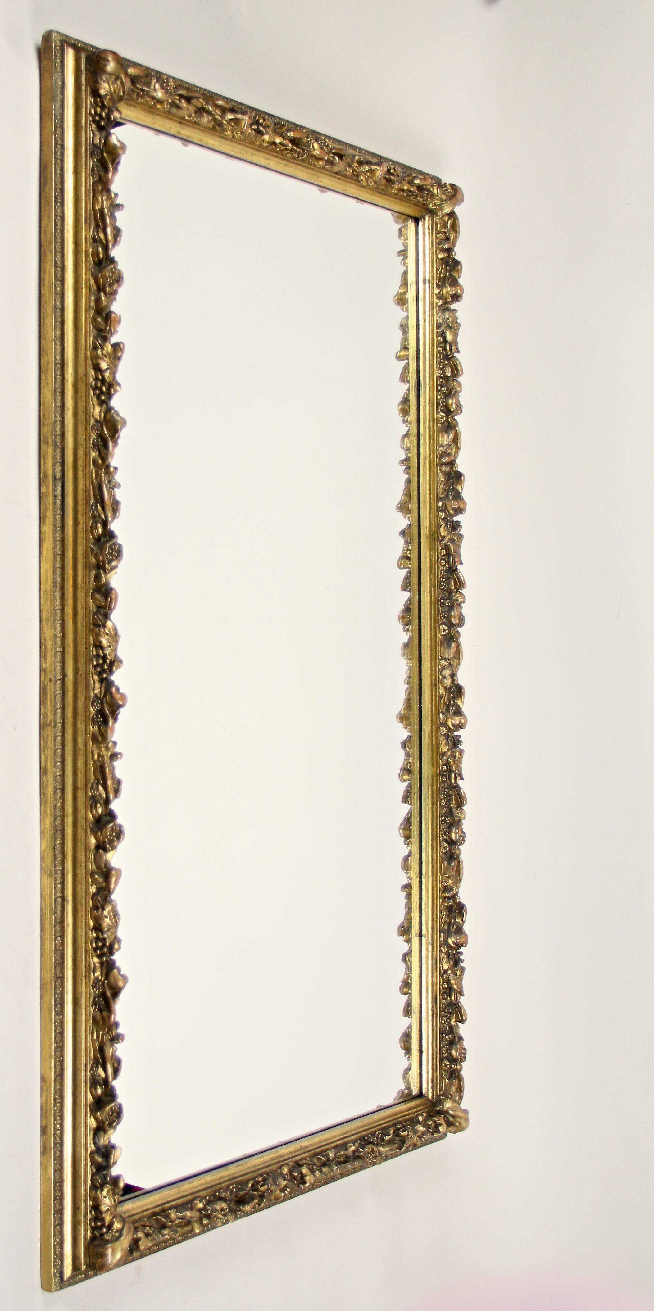 Ravishing floral gilt Biedermeier wall mirror from the 19th century in Austria, circa 1840. This artfully processed large golden wall mirror shows elaborately done stucco works depicting different kinds of fruits and foliage. Gilt with different