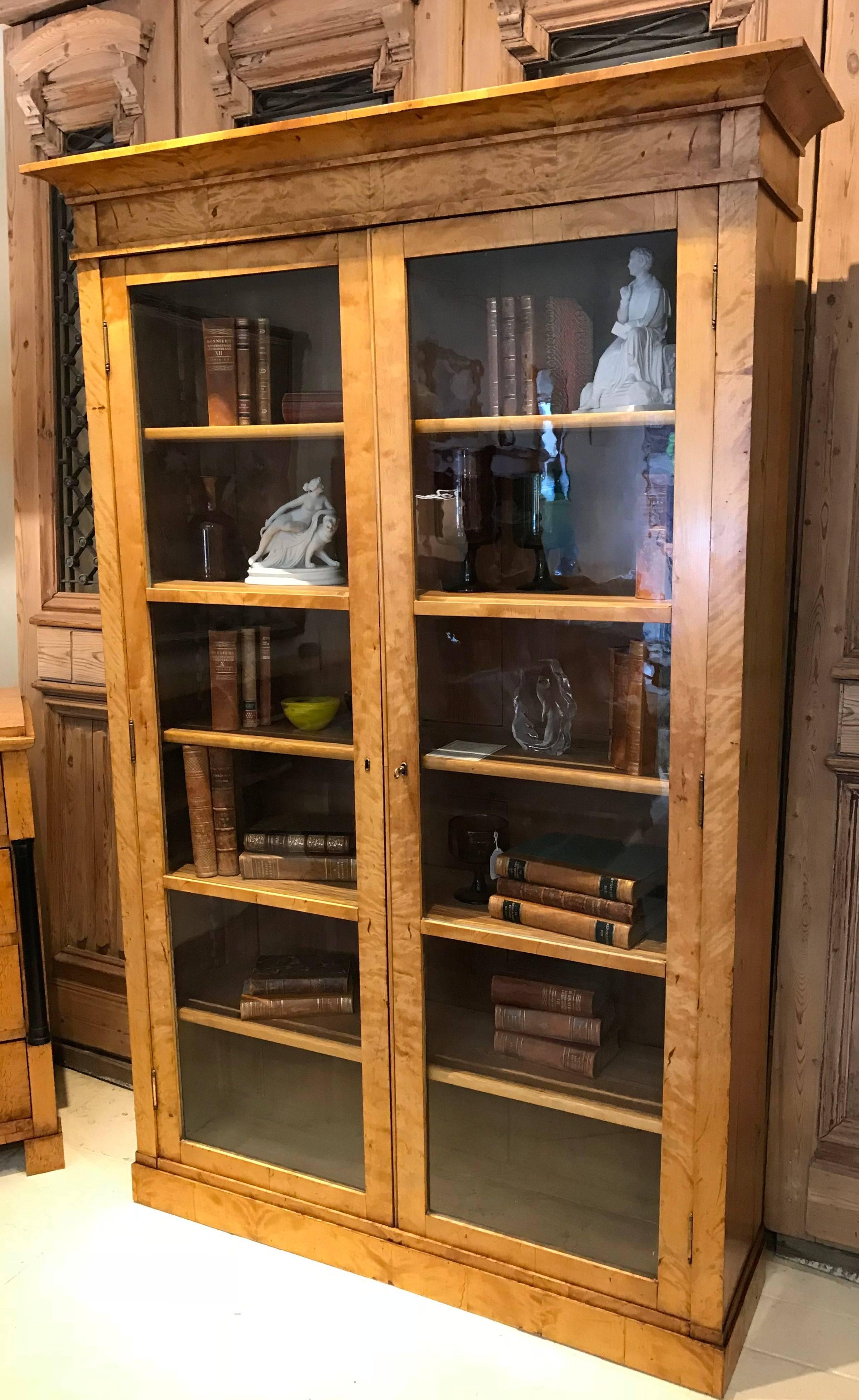 Swedish Biedermeier flame birch glass door bookcase with the original hand drawn glass panes. The shelves are all adjustable. Classical clean lines which are timeless. This bookcase has an elegant simplicity and would blend well into any setting
