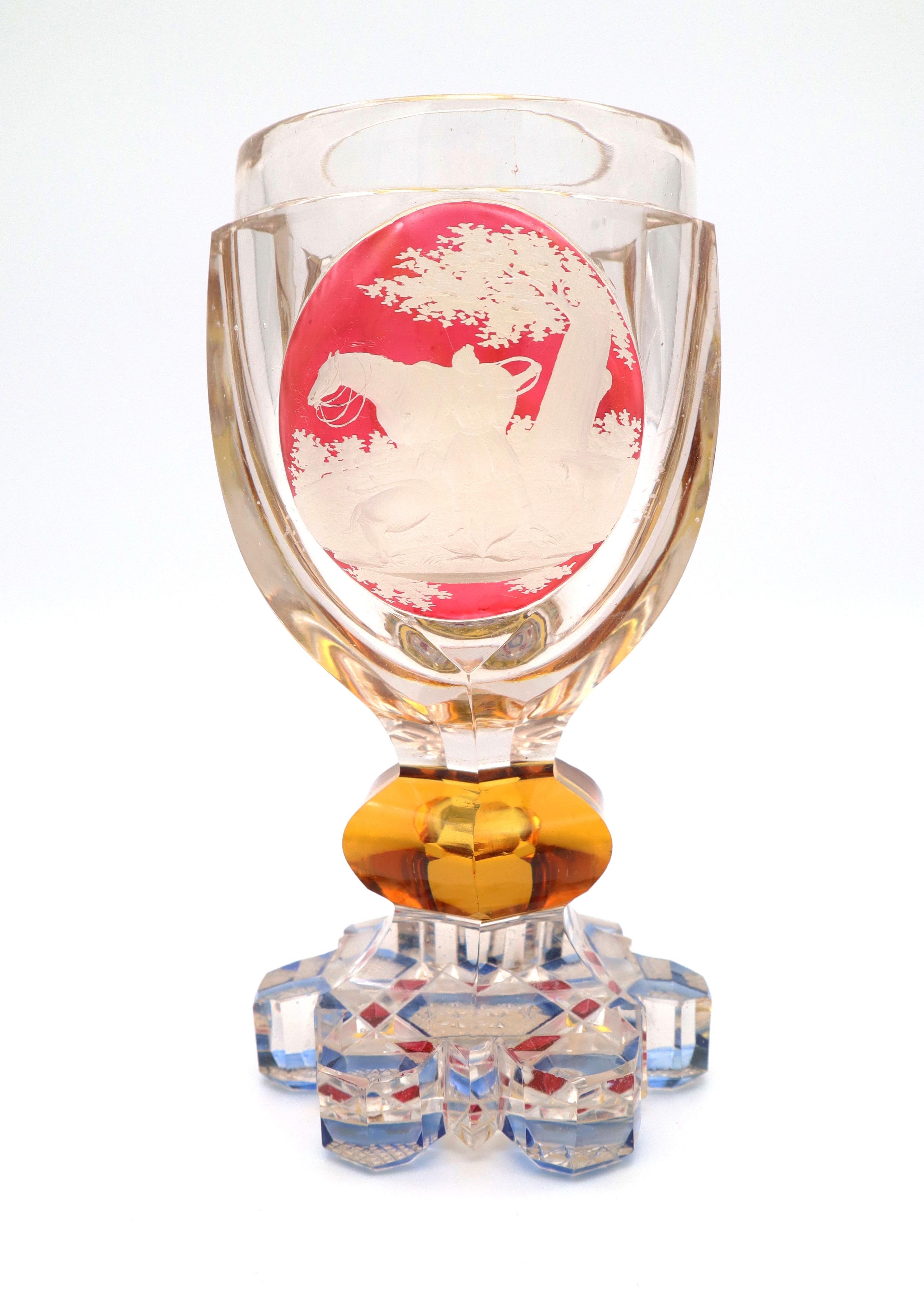 Engraved glass goblet showing a hunt scene on the front, which was accounted for a period of the German and Austrian glass production throughout the eighteenth century.
Its stained, multicolored socket and the star, engraved bottom are typical for