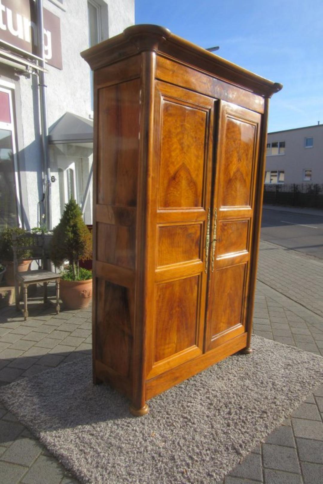 Fantastic Biedermeier hall cabinet or armoire from the 1830s. This unique antique item got crafted out of luxurious walnut wood and therefore features a beautiful colored veneer. French cabinet with elegant brass details. It is in a perfect