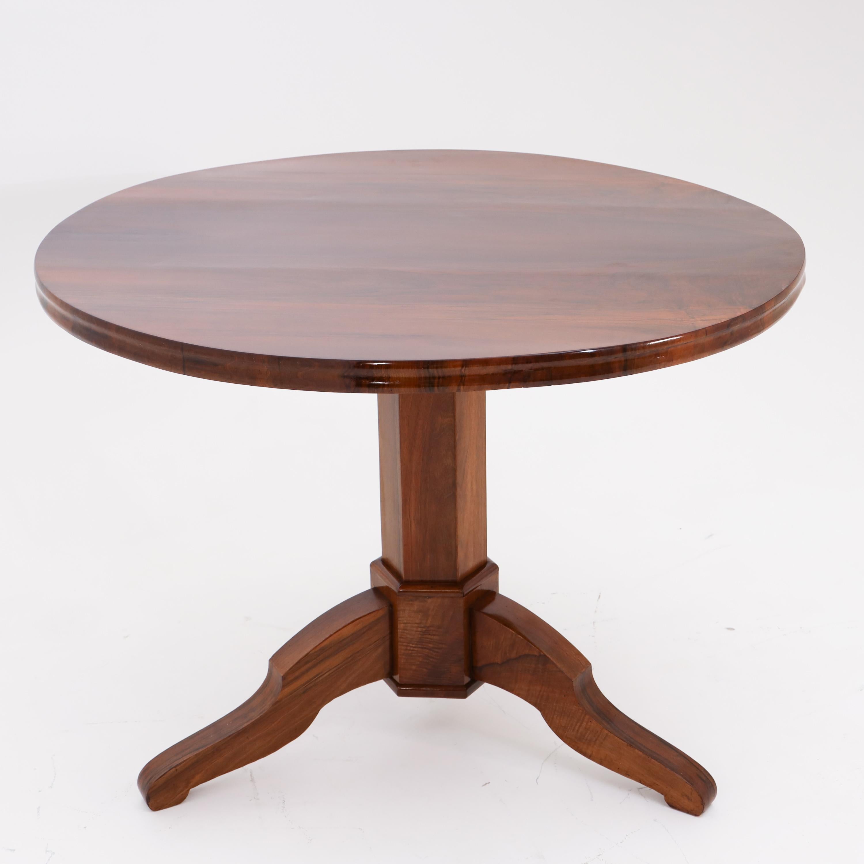 Biedermeier salon table on three S-shaped legs around a hexagonal column base and a round tabletop with a slight chamfer.