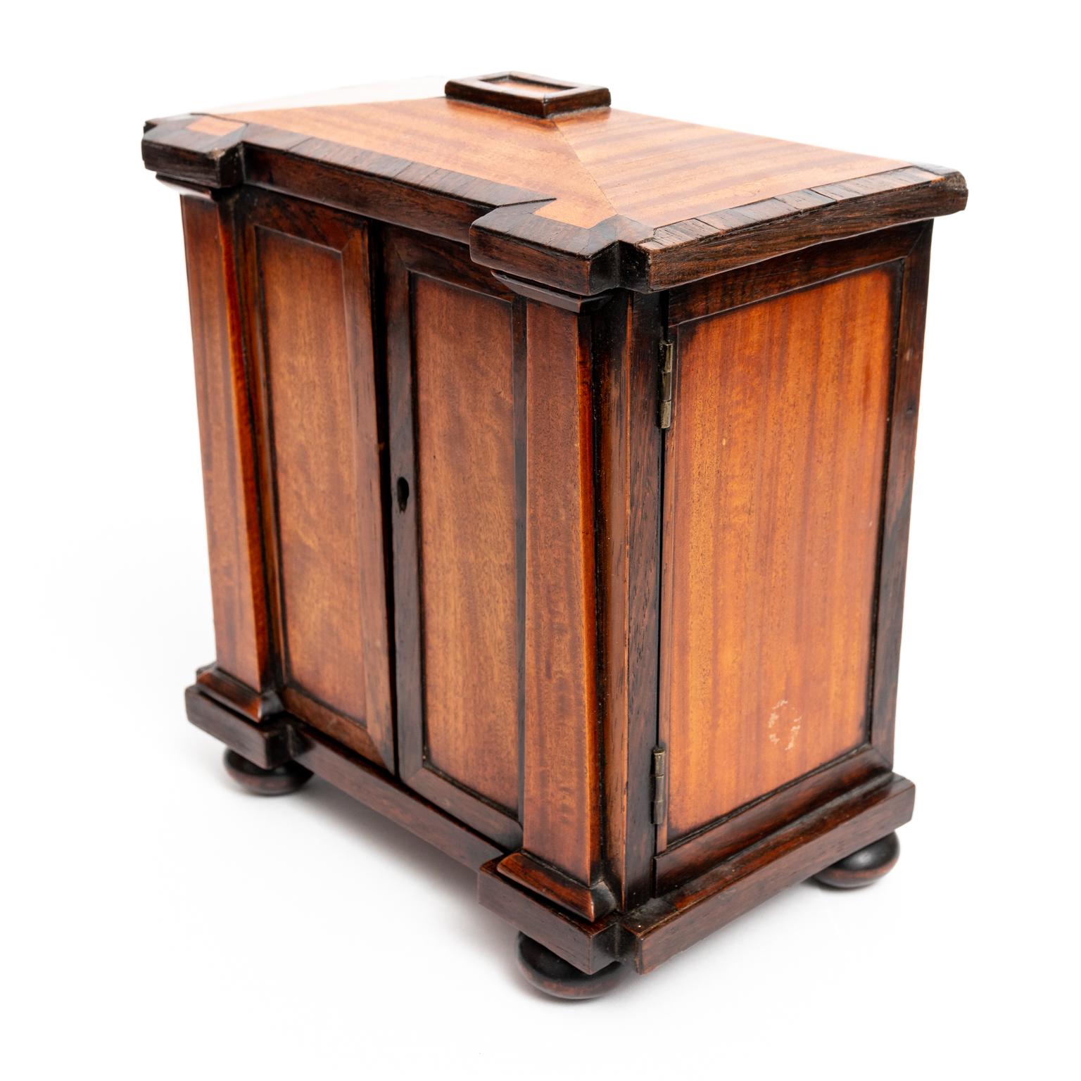 Circa 1820s Continental Biedermeier style four drawer miniature chest of drawers in Satinwood and Rosewood. The piece is constructed with two panel front doors flanked by Tuscan columns and supported by bun turned feet. Please note of wear