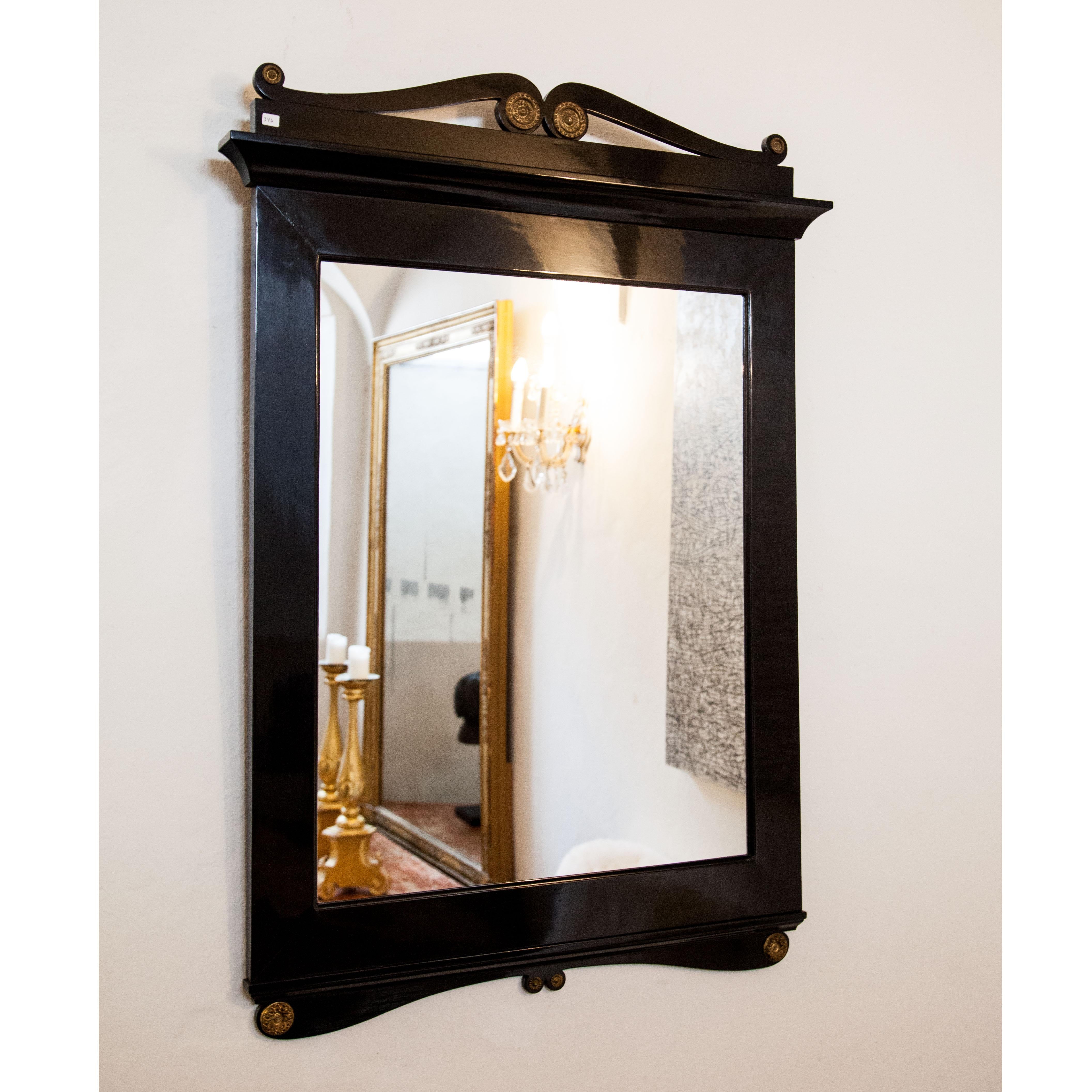 Biedermeier mirror in smooth ebonized wooden frame with rocaille decoration and bronze rosettes.