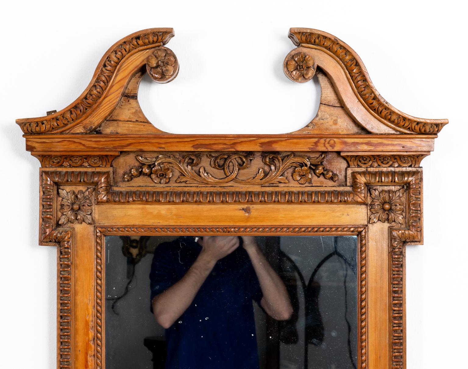 Circa late 19th century Biedermeier style mirror in carved wood with top broken scroll pediment detail. The piece is also heavily decorated with motifs such as scrolled foliage underneath the pediment, dog ear corners, and rope trim surrounding the