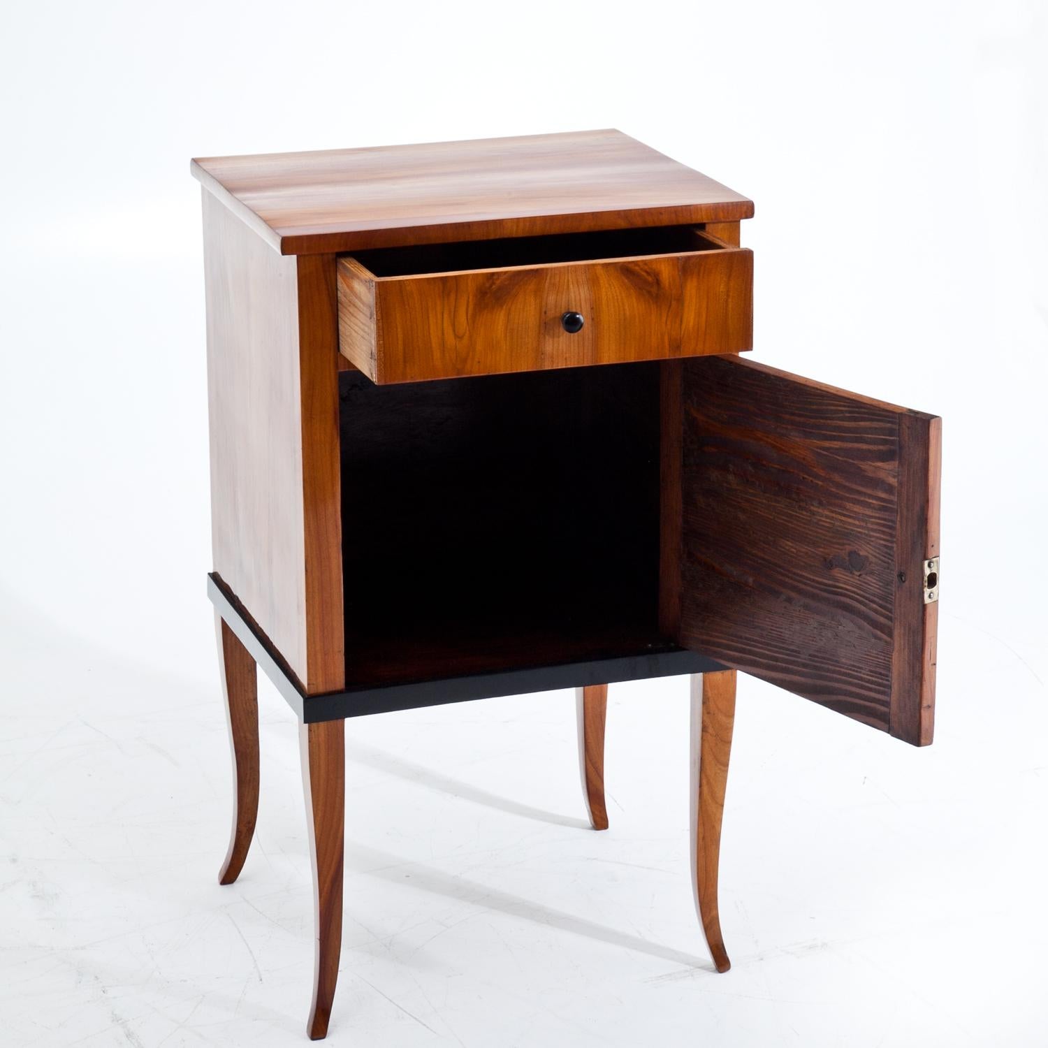 Small cherrywood nightstand standing on S-shaped legs with one door and one drawer. The knobs are ebonized.