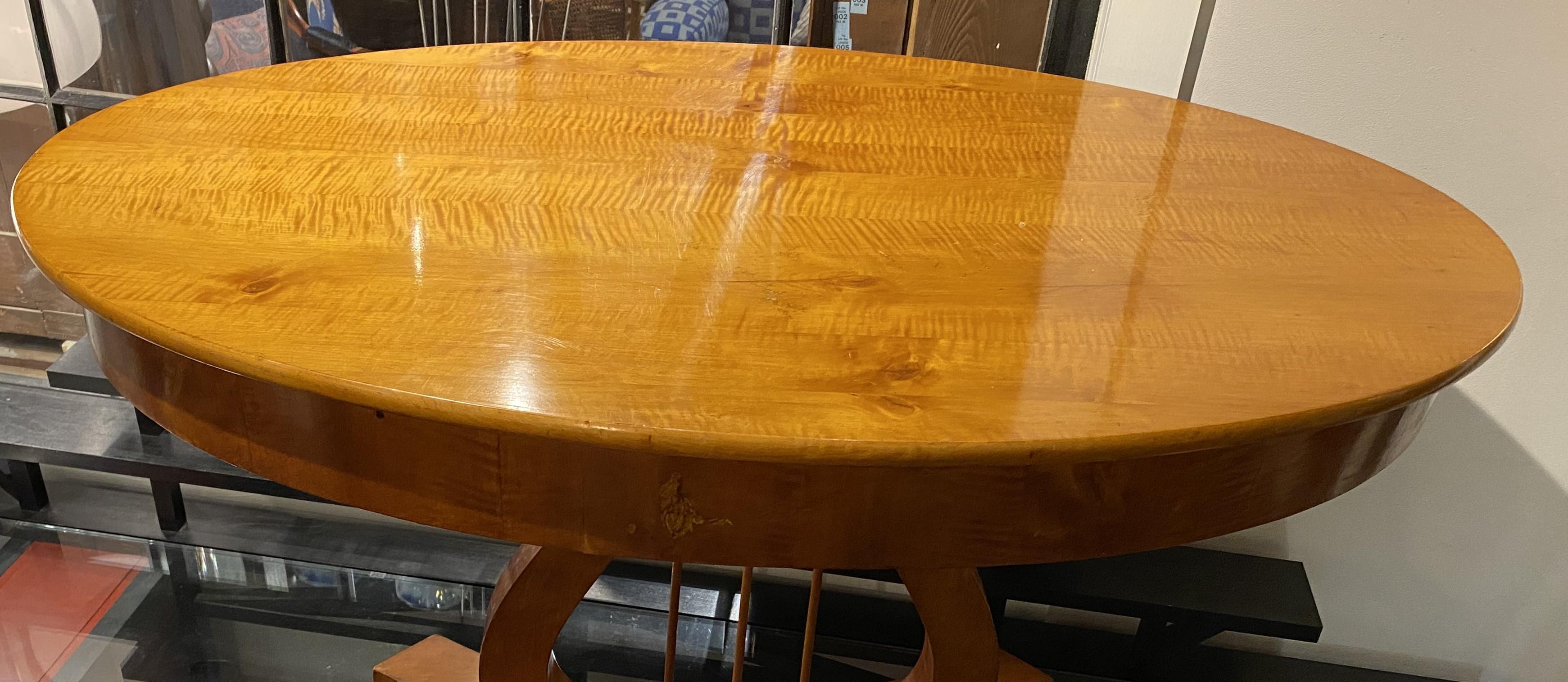 A fine Biedermeier or Classical style oval center table in curly maple with scroll carved lyre form pedestal on a shaped base with four outstretched feet. Dates to the 19th century in very good condition, with great tiger maple wood grain, minimal