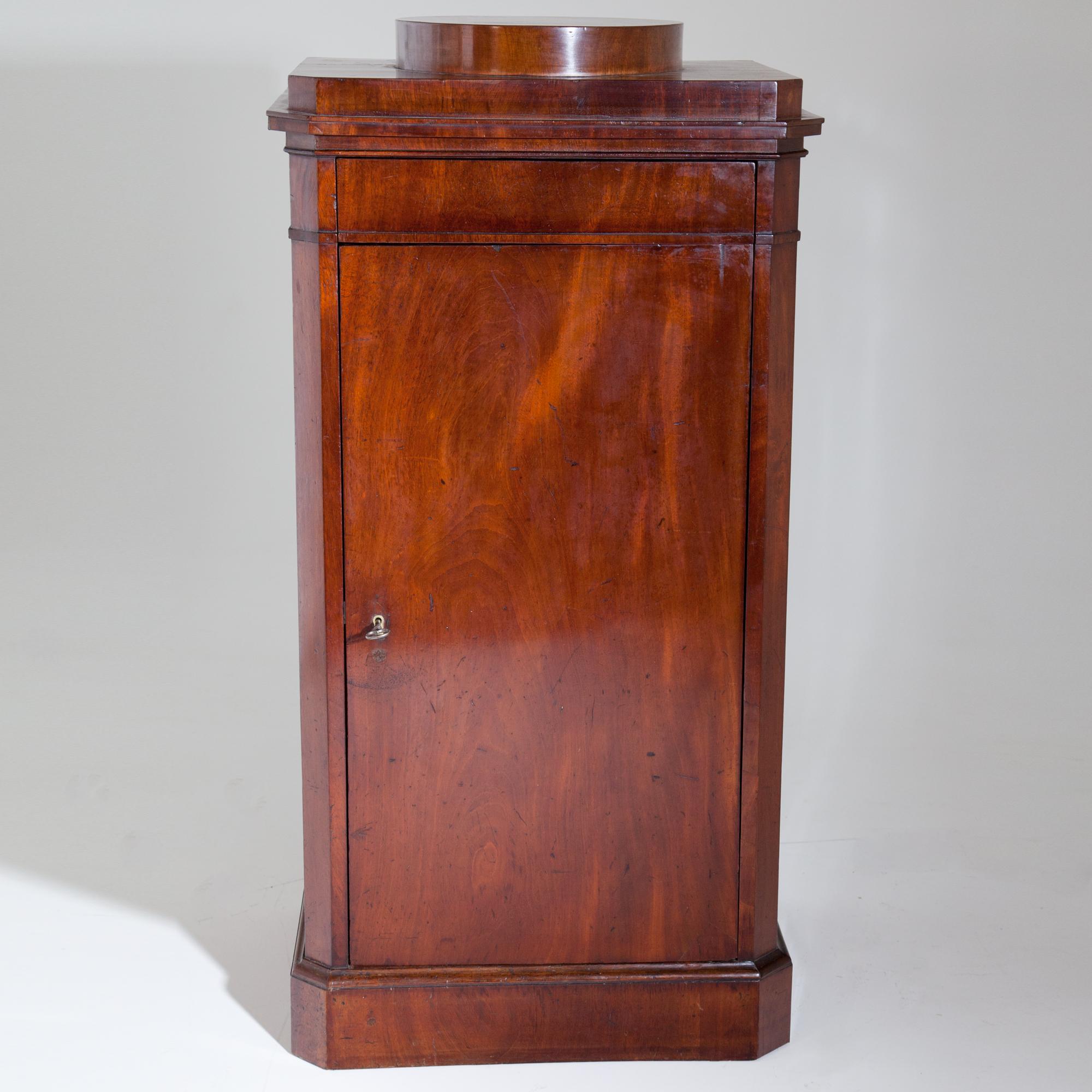 Single-door mahogany pedestal with light base and beveled corners. Shelf with round platform (6 x Ø34 cm). The interior layout consists of three shelves.
