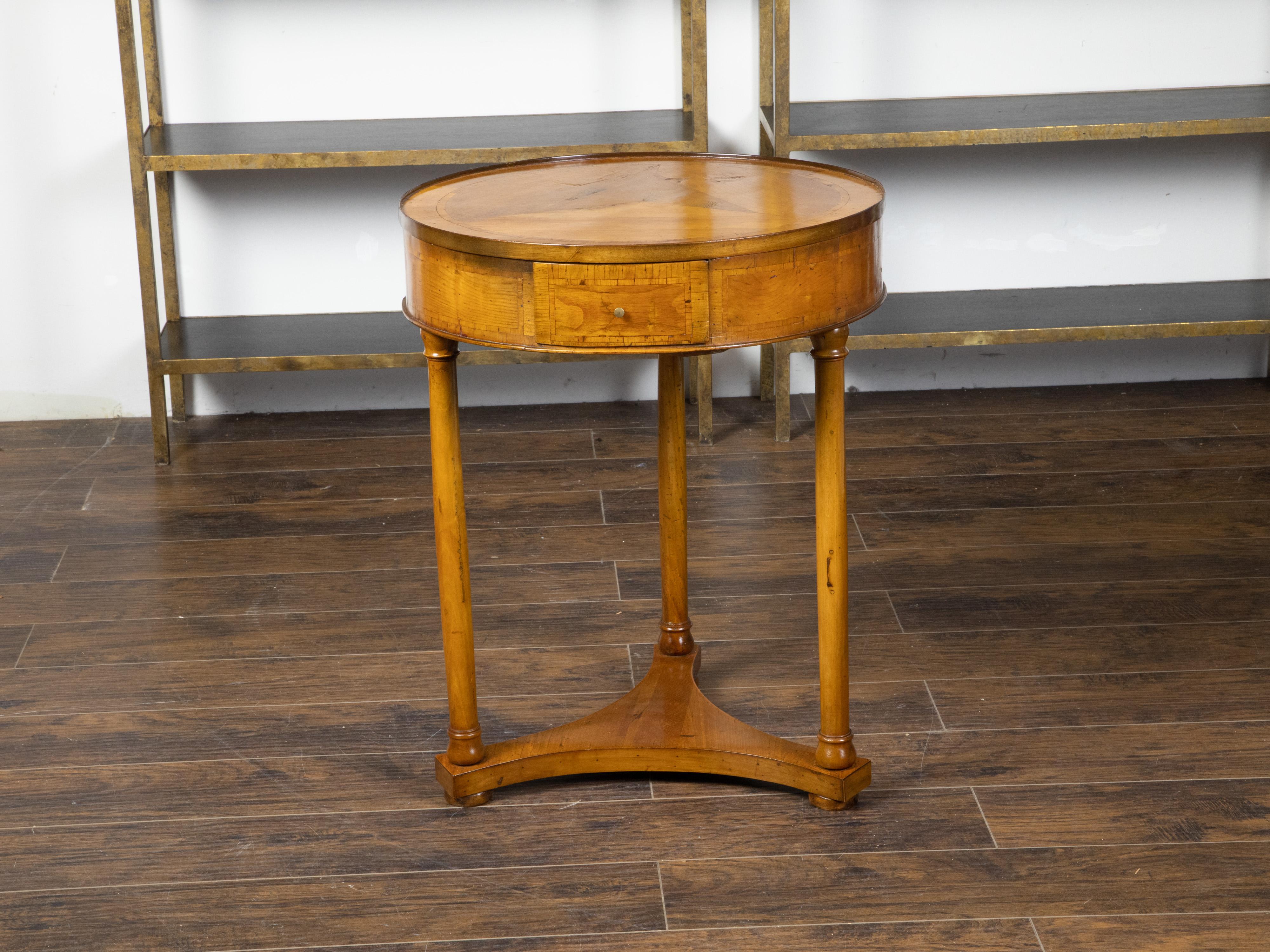 An Austrian Biedermeier period side table from the mid 19th century, with veneered top, banding, three drawers and column legs. Created during the Biedermeier period, this table features a circular veneered top sitting above an elegant apron