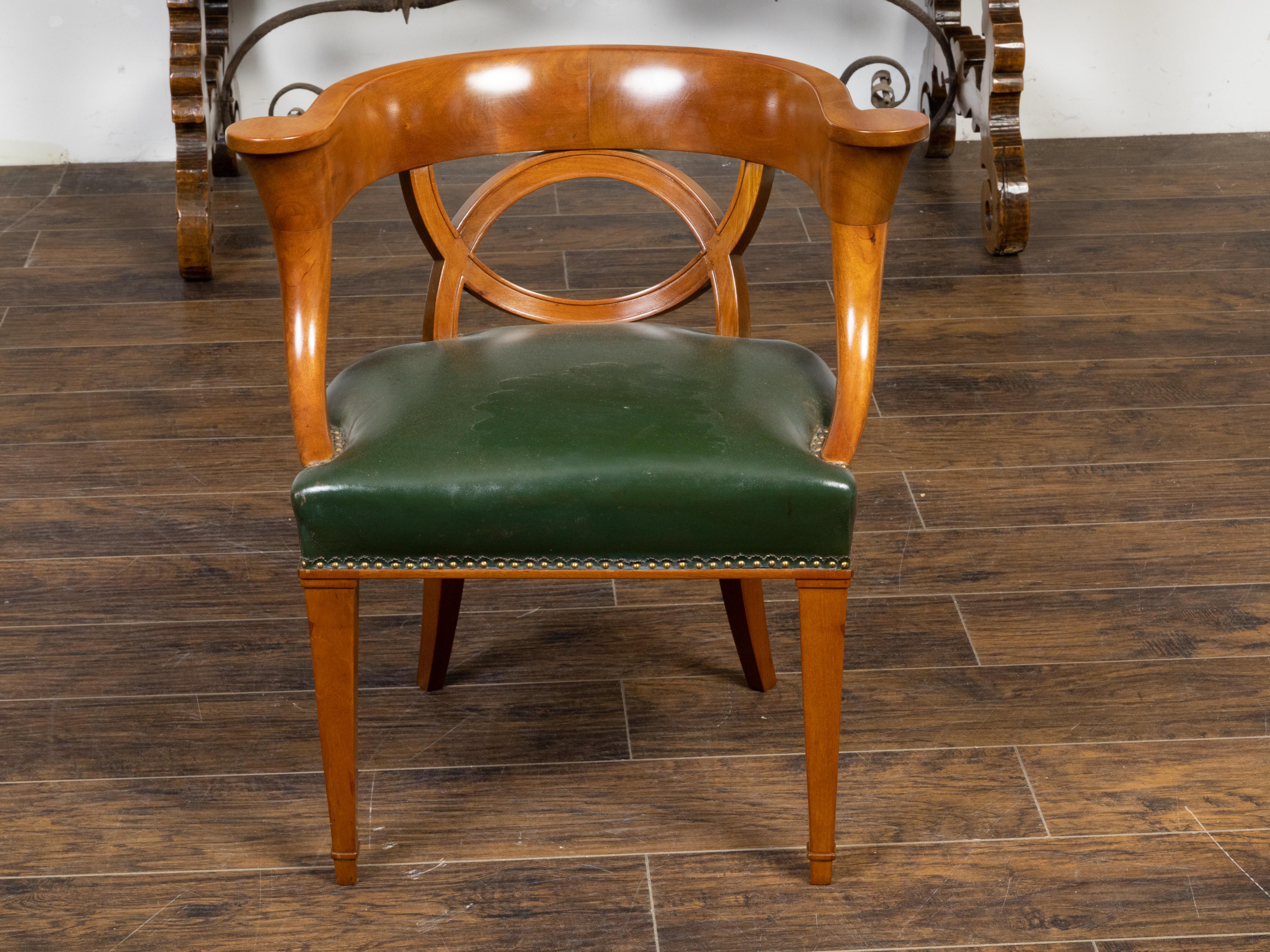 An Austrian Biedermeier period wooden armchair from the 19th century, with unusual horseshoe back, out-curving arms, intertwined semi-circular motifs, turned and saber legs and green leather upholstery. Created in Austria during the 19th century,