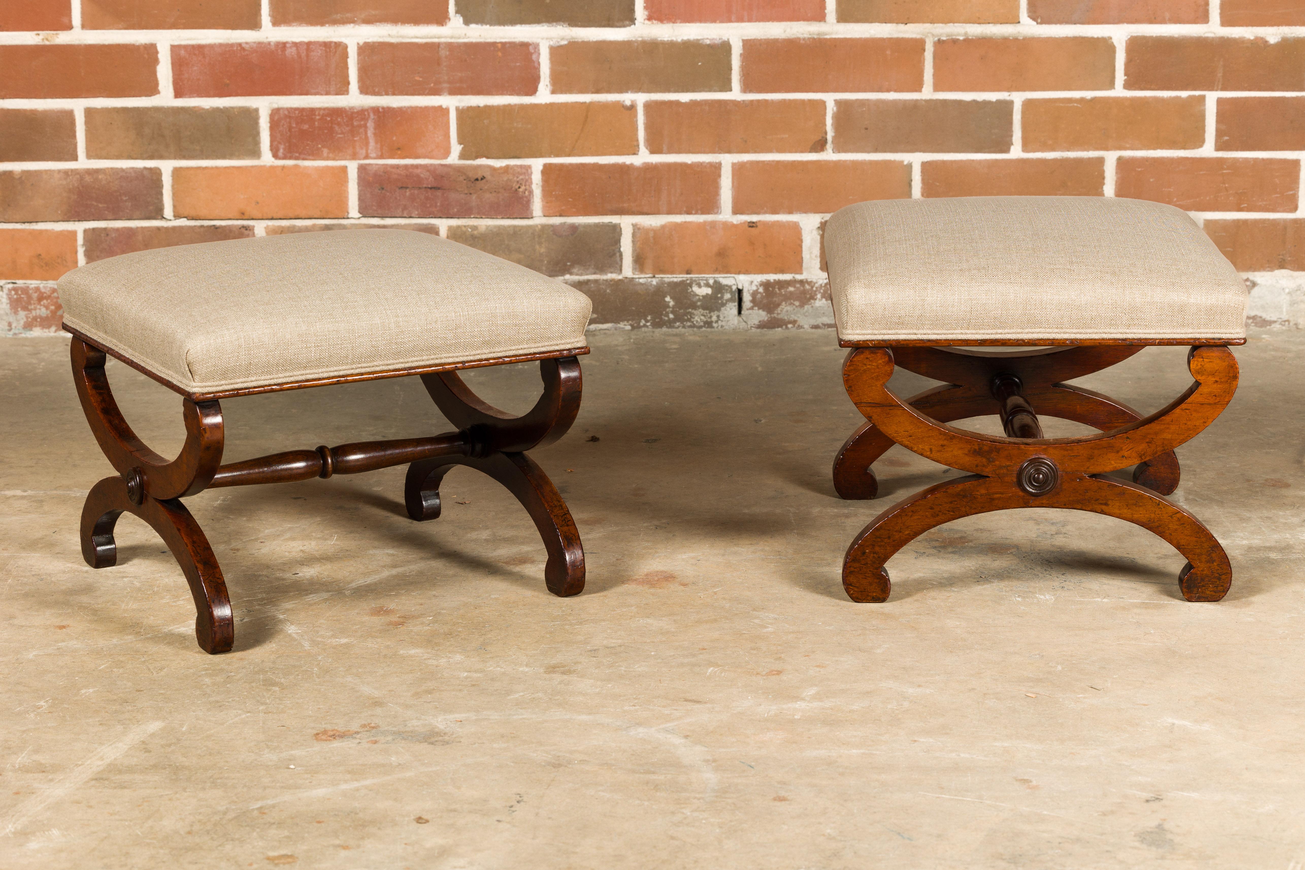 A pair of Biedermeier period walnut stools from the 19th century with X-Form bases, turned spindle shaped stretchers and upholstered seats. These 19th-century Biedermeier walnut stools are an embodiment of classic elegance and timeless design.
