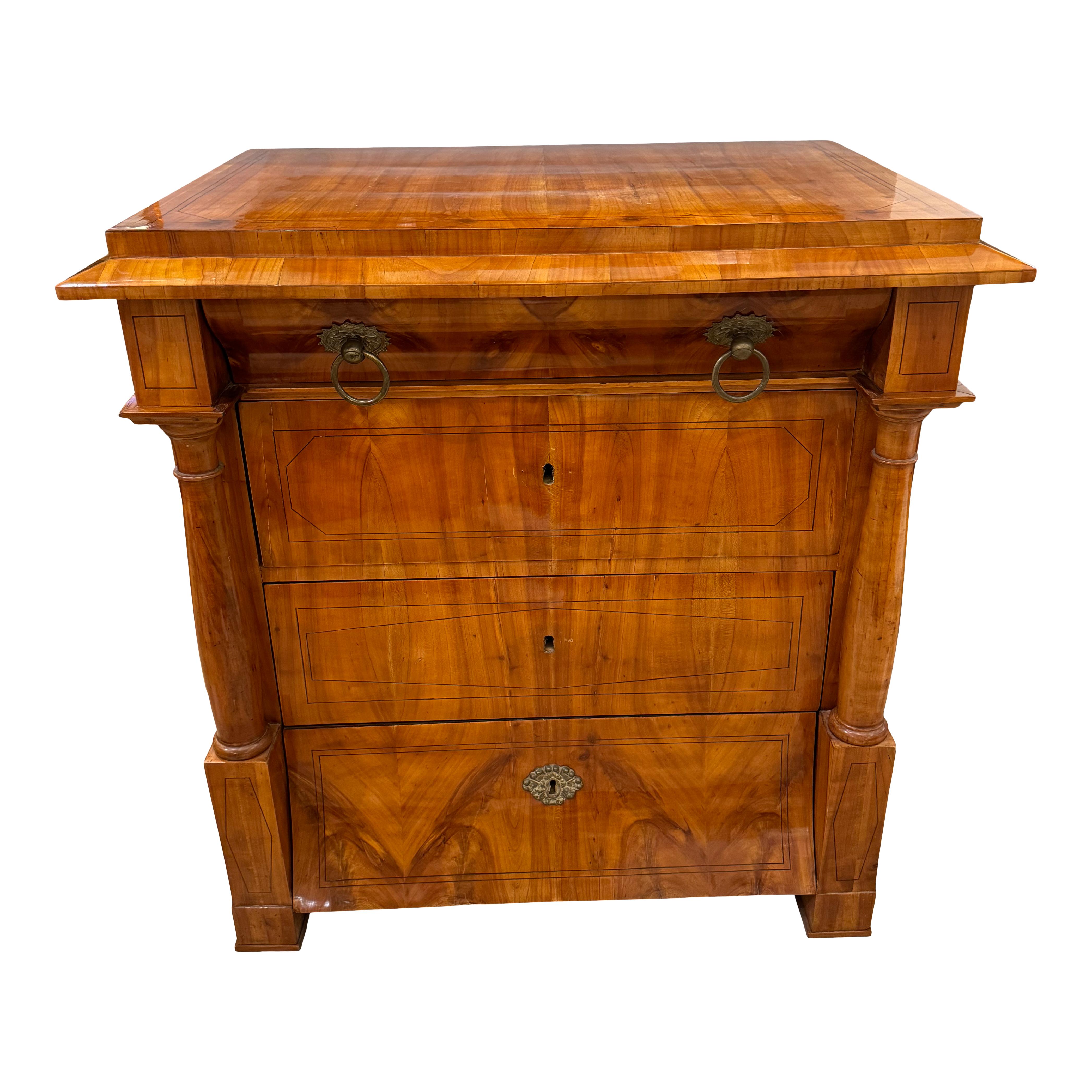 Fina cómoda de cuatro cajones de la época Biedermeier, procedente de Austria, hacia 1820. Madera de cerezo con incrustaciones de ébano y tiradores de bronce.