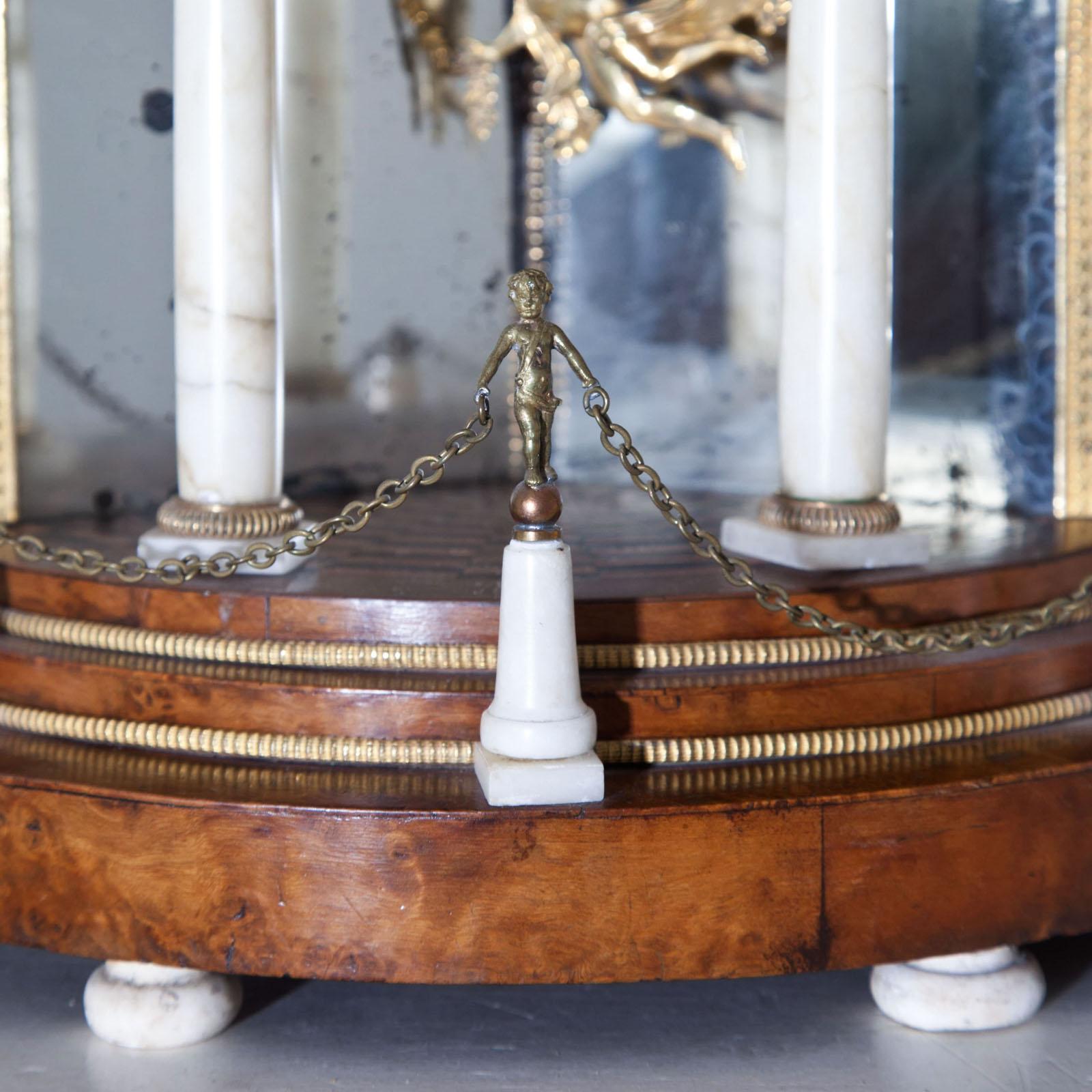 Biedermeier portal clock in an architecturally structured walnut case with alabaster columns, bronze fittings and mirrored rear wall. The clockwork with date and sound spiral. Pendulum in the shape of a winged putto.