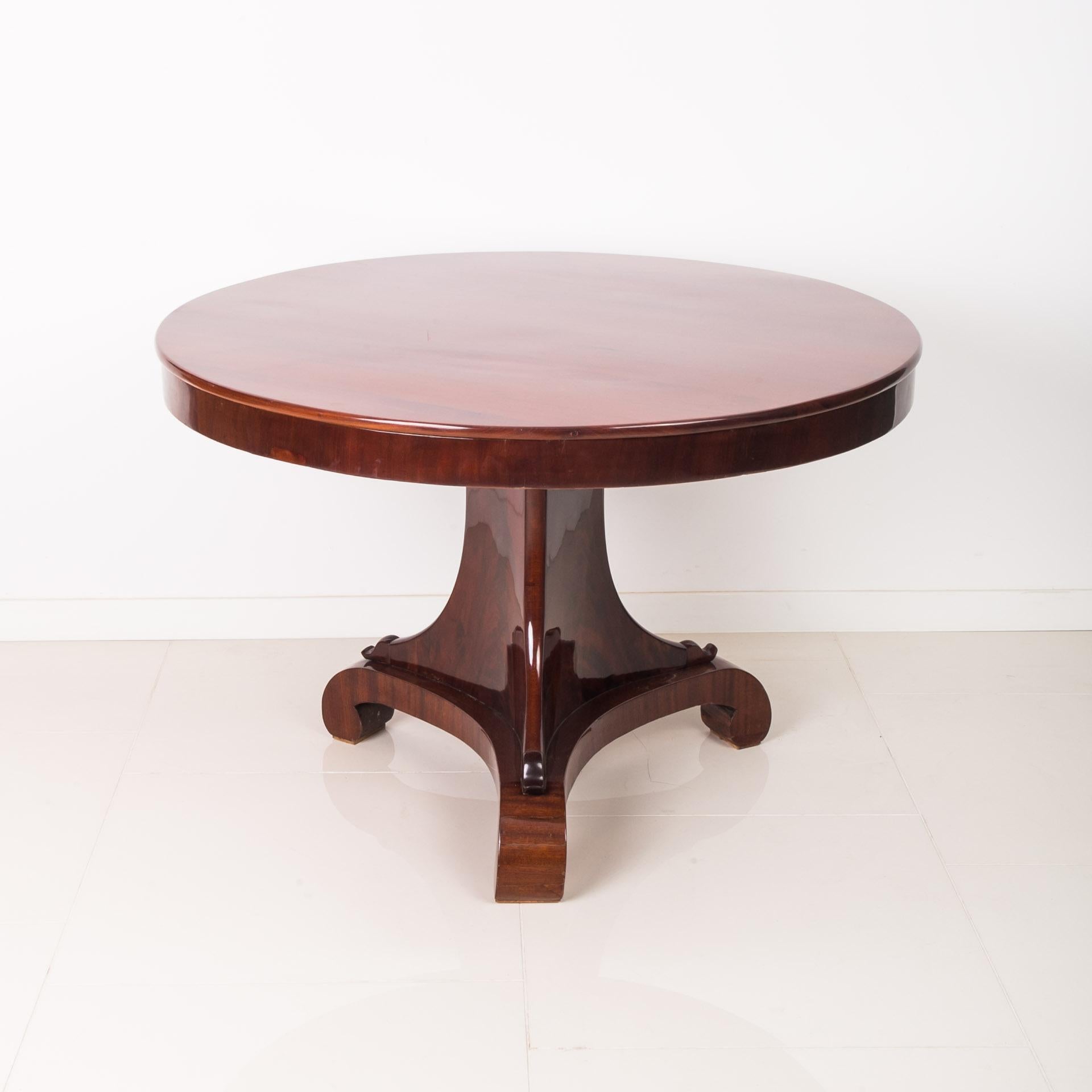 This Biedermeier round table was made around 1820 - 1840. It is supported on a trilateral shaft with rounded corners extending downwards, placed on a triangular platform. The piece is made of coniferous wood and veneered with pyramidal mahogany, the