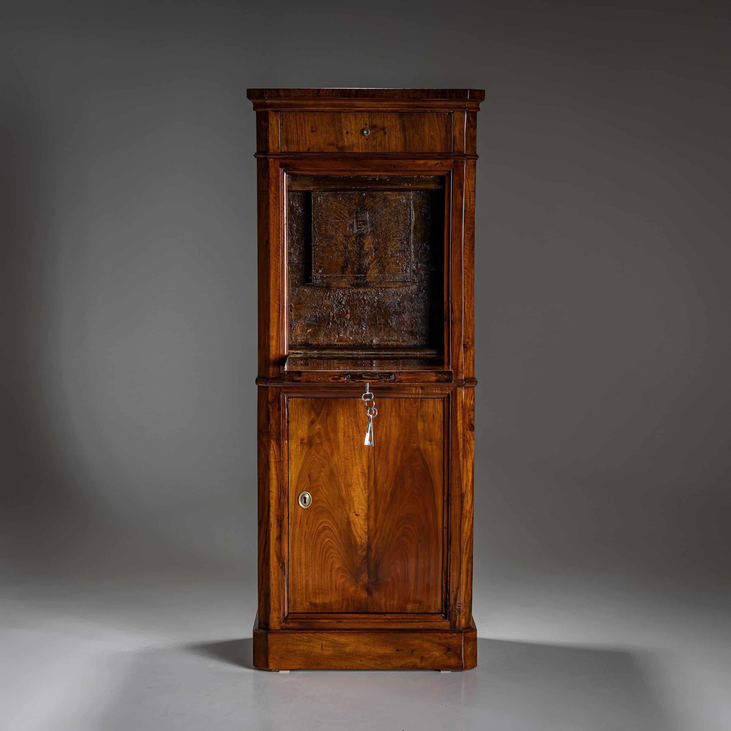 Außergewöhnlicher Biedermeier-Tresorschrank mit einem eintürigen Unterteil, einer flachen Klappe und einer oberen Schublade. Der Korpus mit abgeschrägten Ecken ist elegant strukturiert und mit Zierleisten versehen. Der Clou an diesem Stück ist der