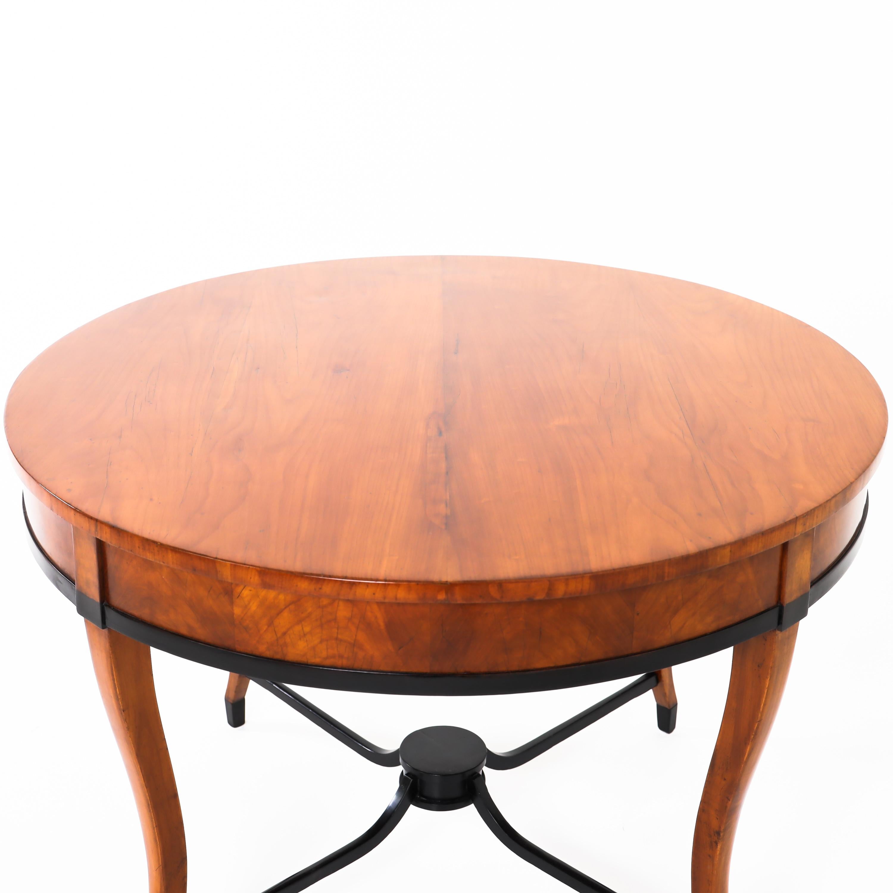 Biedermeier salon table in cherry with ebonized bracing. The s-shaped legs stand on feet also ebonized (recent).