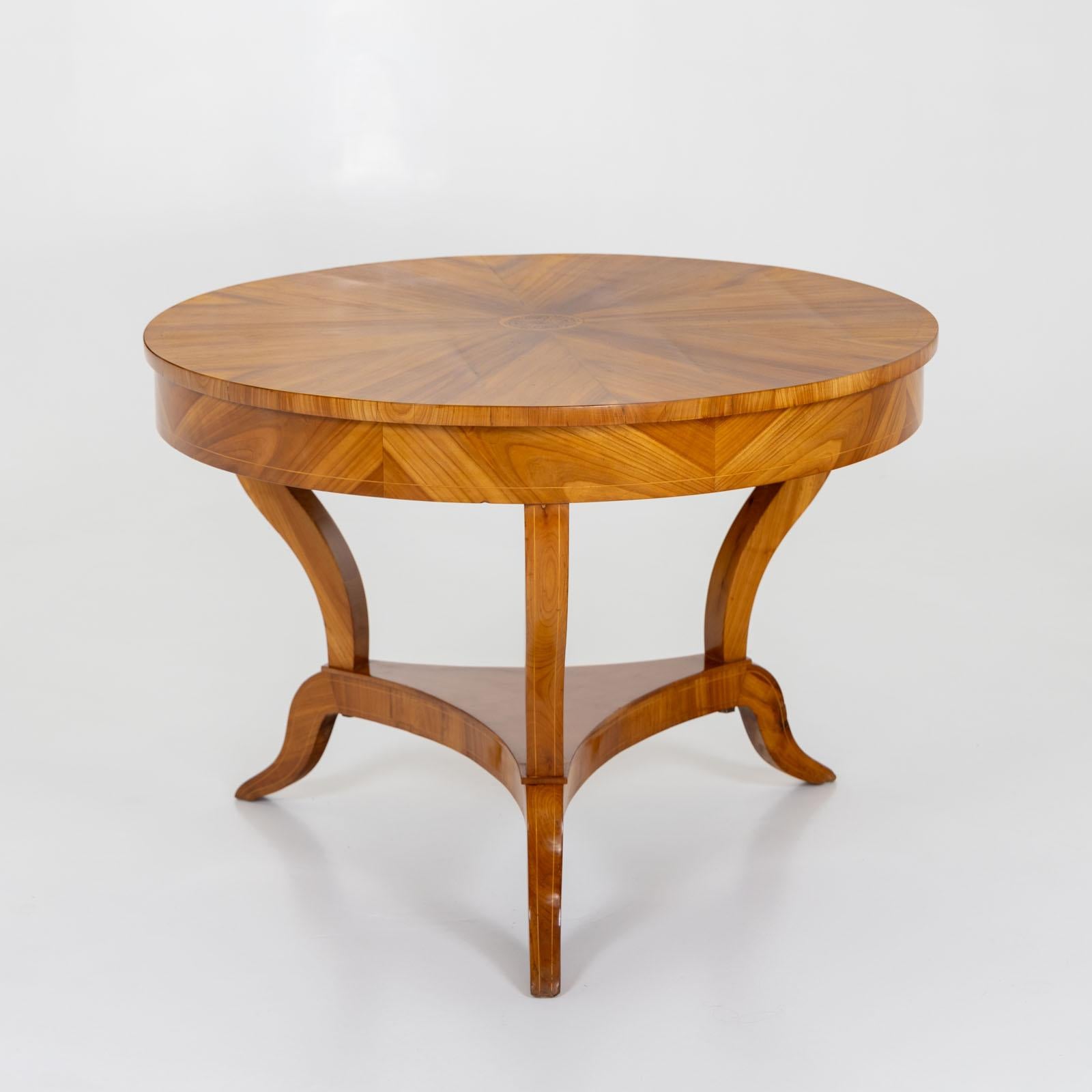 Large Biedermeier salon table on three legs with retracted central column and smooth frame. The radial veneered table top is inlaid in the middle with a stylized floral pattern, the frame and legs are set off with light thread inlays. The table is