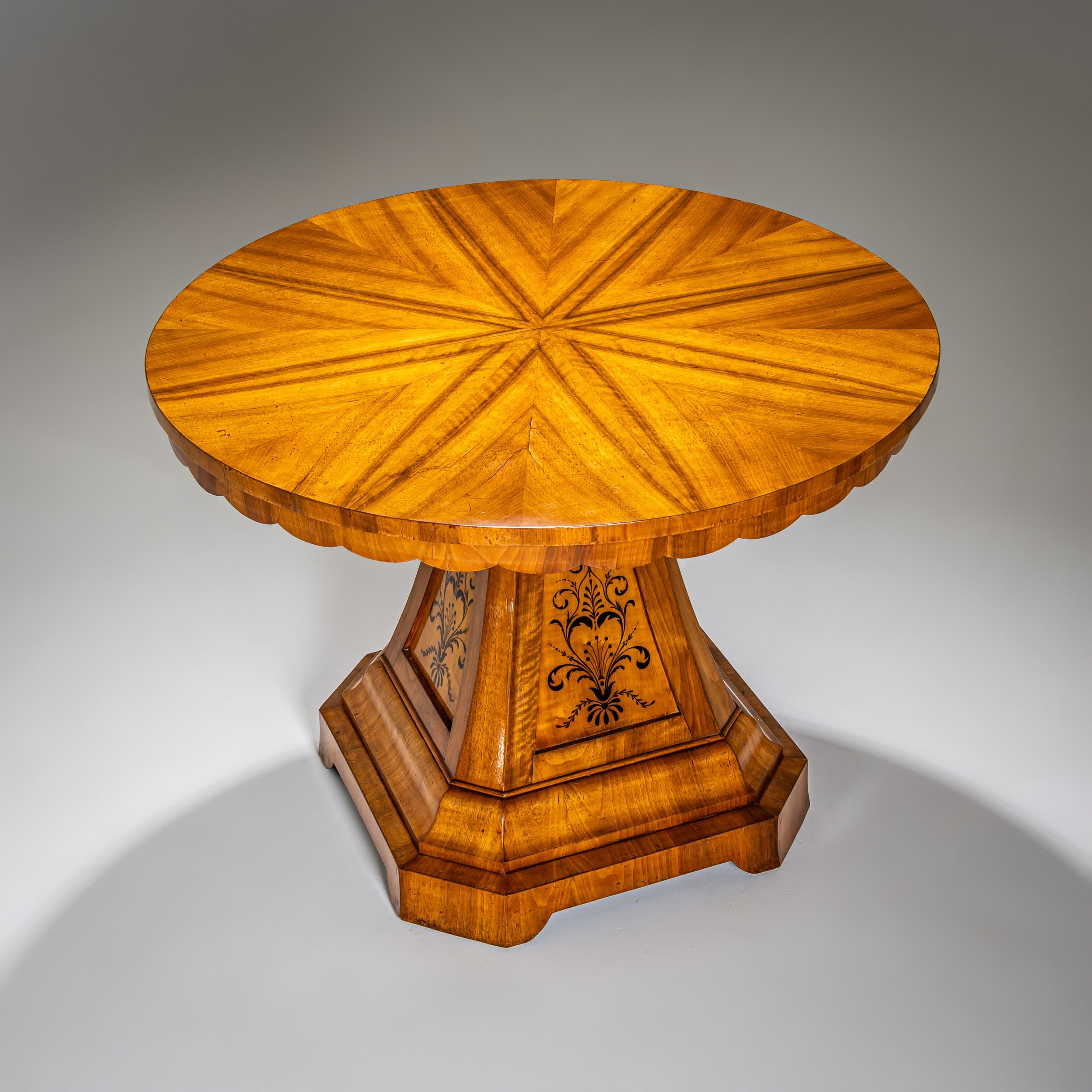 Large salon table with a round top and gently scalloped apron. The bold, pyramidal central pedestal stands on an octagonal base. The sides are adorned with delicate floral inlays. Veneered in cherrywood, professionally restored and hand-polished.
