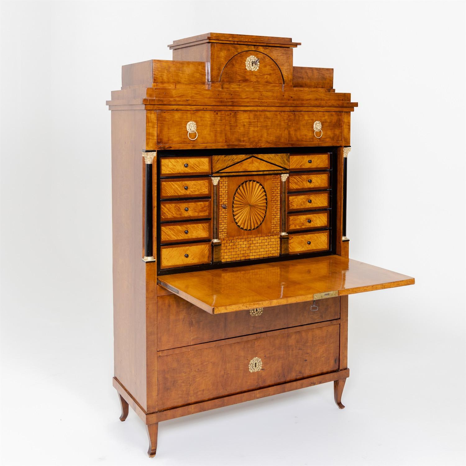 A straight corpus with folding writing flap and wide top drawer rises above a two-drawer base, standing on slightly outwardly curved square feet and is crowned by a stepped pediment with one drawer and segmental arch decoration. The ebonized half