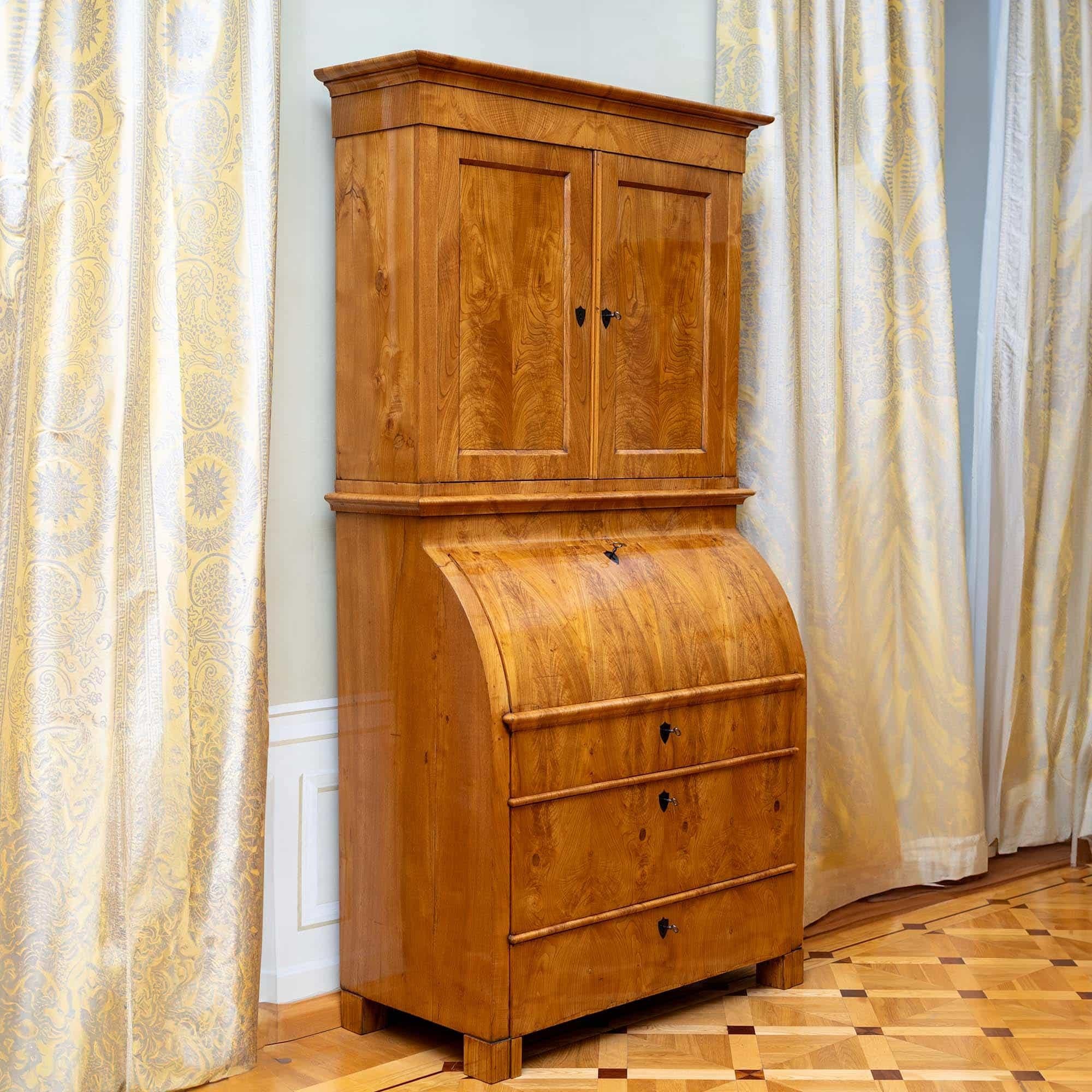 Spacious secretary featuring a two-door cabinet top and a three-tier chest of drawers base. The secretary is veneered with ash and meticulously hand-polished to highlight its natural beauty. The curved writing surface unveils an interior with a