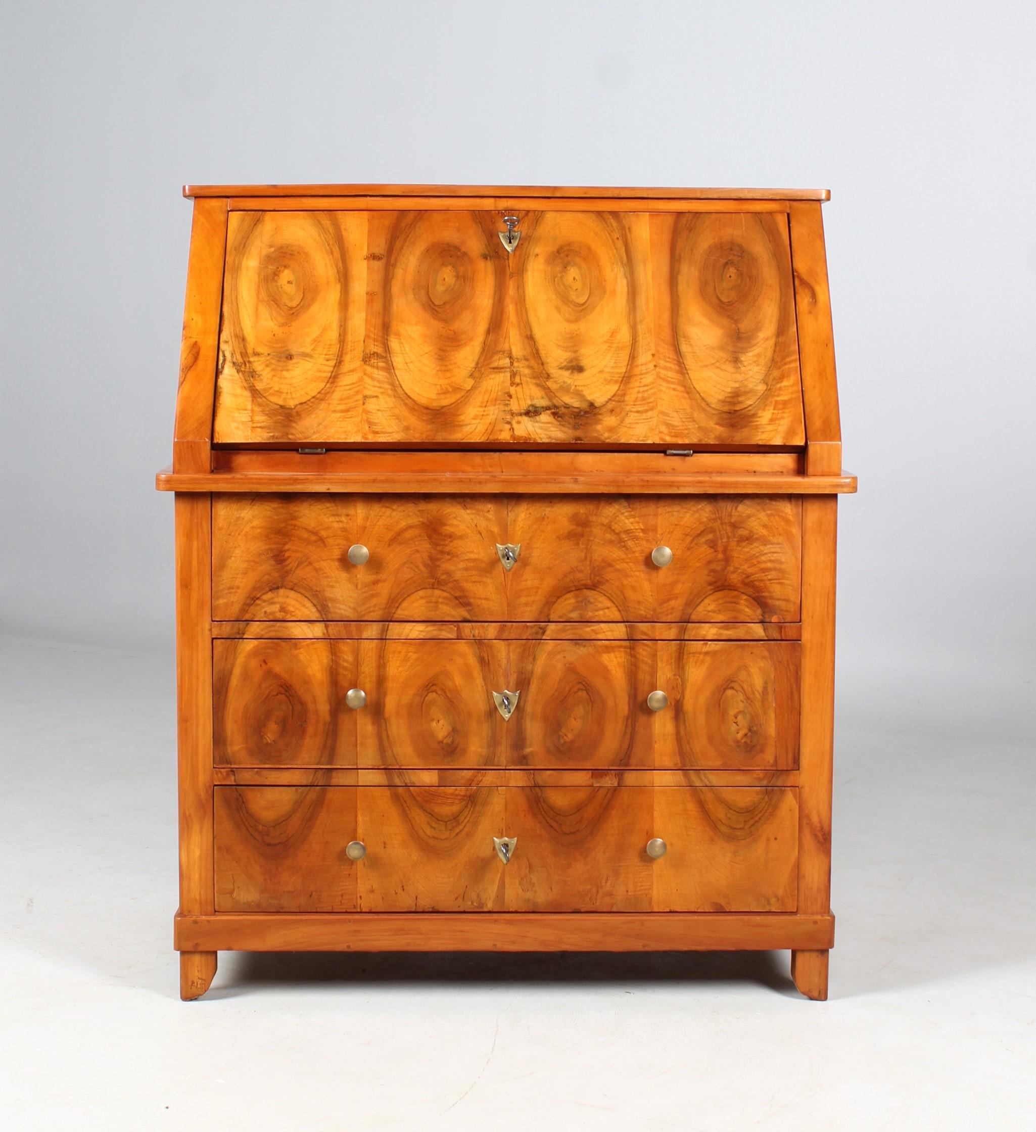Antique cabinet secretary from the biedermeier period around 1845.
Body in cherry, parts of the front and the wreath veneered in walnut. Handles and fittings made of brass in the shape of coat of arms.

The secretary can be disassembled into
