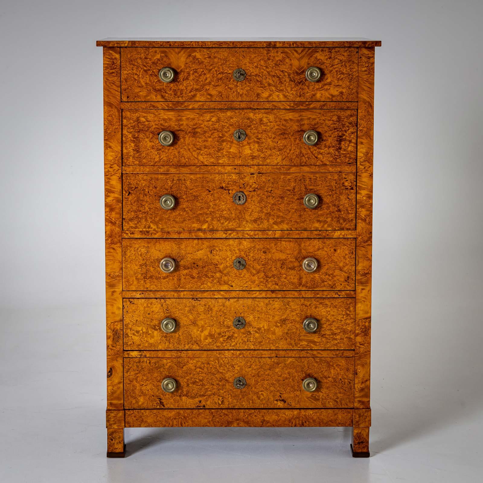 Escritorio de secretaria Biedermeier en forma de cómoda alta sobre patas cuadradas. El secreter está chapado en raíz de tuya y equipado con herrajes de bronce. El secreter cerrado parece estar equipado con seis cajones. Detrás del segundo y tercer