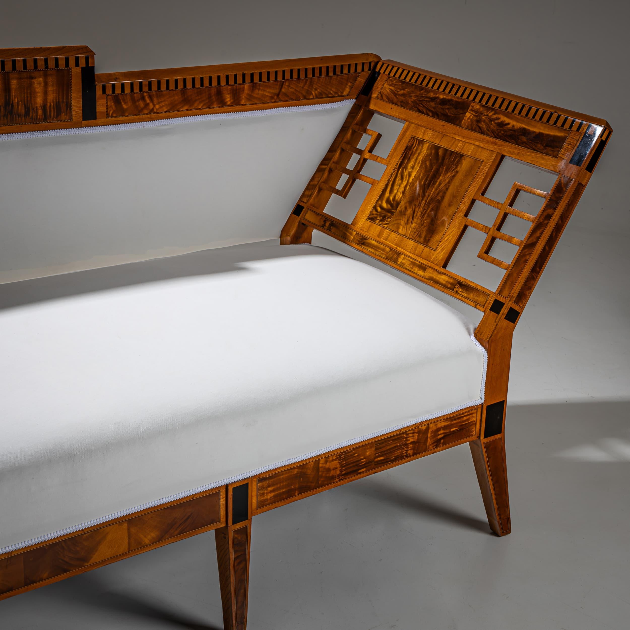 Elegante divano in legno di frassino con pannelli laterali traforati e uno schienale dritto e accentuato ornato da una raffinata decorazione a intarsio. Rivestito in un tessuto semplice e neutro che esalta la sobria eleganza tipica del primo design