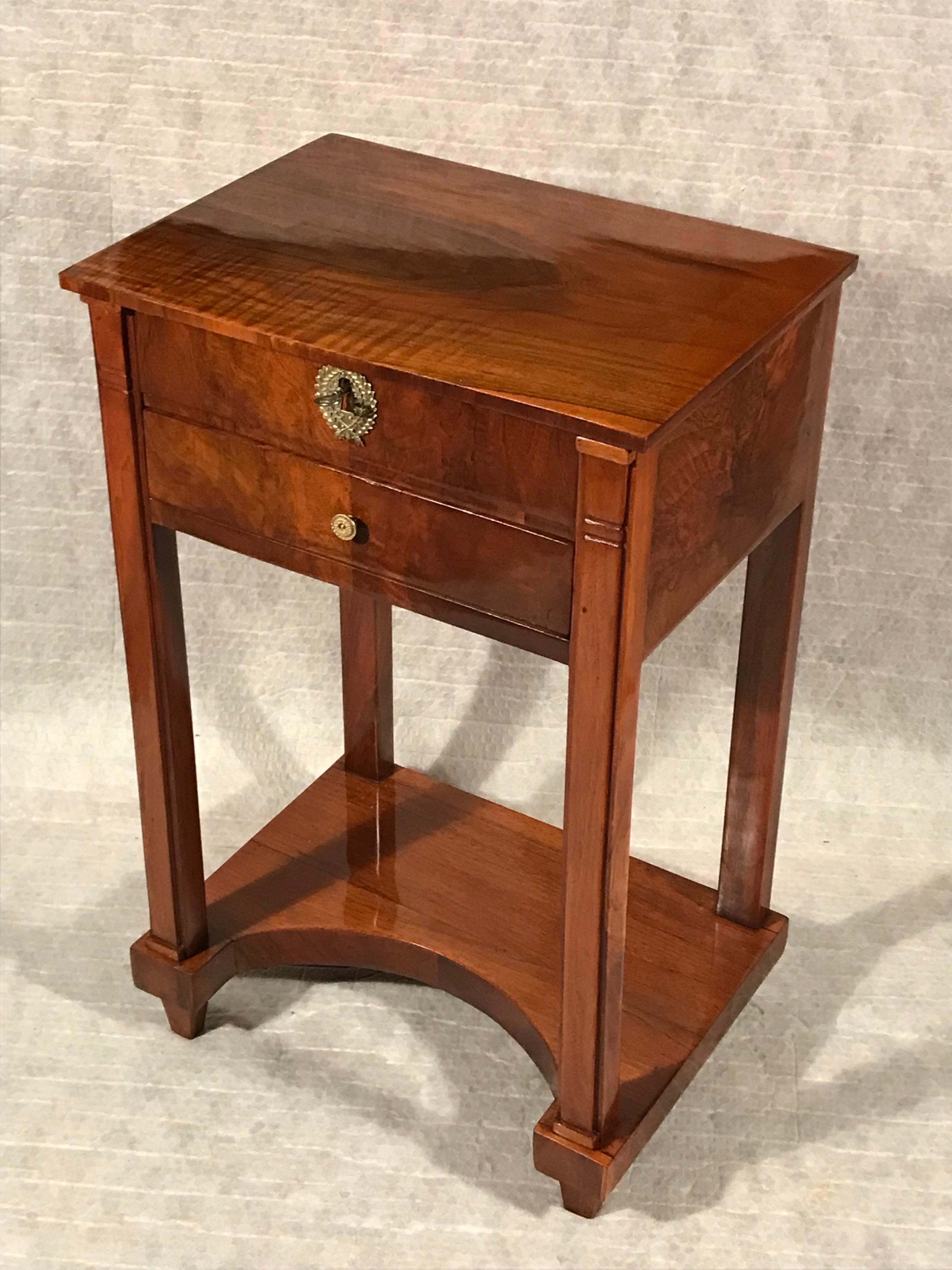 Esta exquisita mesa auxiliar o de costura Biedermeier data de 1820 y procede del sur de Alemania. La antigua mesa Biedermeier original se sostiene sobre cuatro patas cuadradas. La base de diseño cóncavo, el tablero, el frontal y los laterales de la