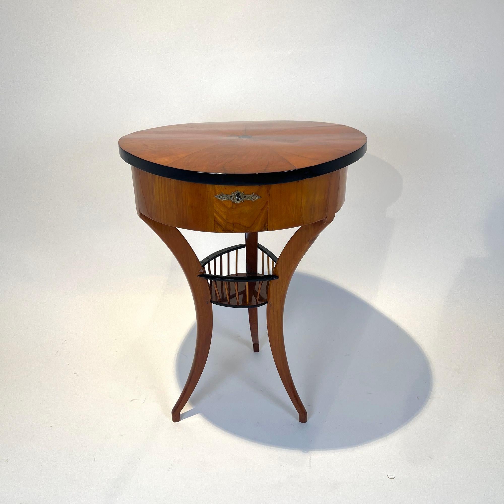 Small, round, three-legged Biedermeier sewing table with flap from Southern Germany around 1820.

Cherry veneered and solid, partly ebonized. Three-legged with intermediate tableau and rung railing.
Original brass fittings and iron lock. Interior