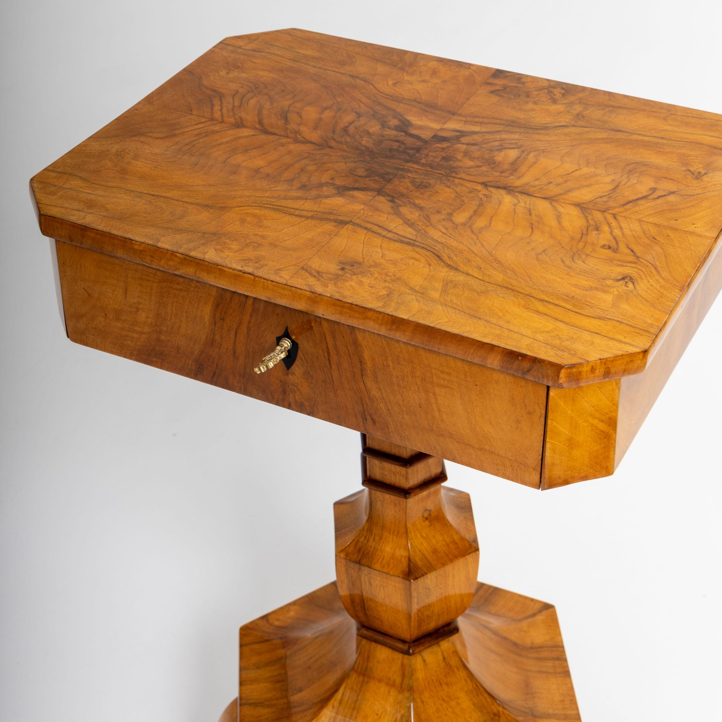 Elegant Biedermeier sewing table in walnut with an octagonal tabletop and a single drawer. The vase-shaped, hexagonal pedestal base stands on three curved legs. The drawer features a compartmentalized interior and a fold-out pincushion, reflecting