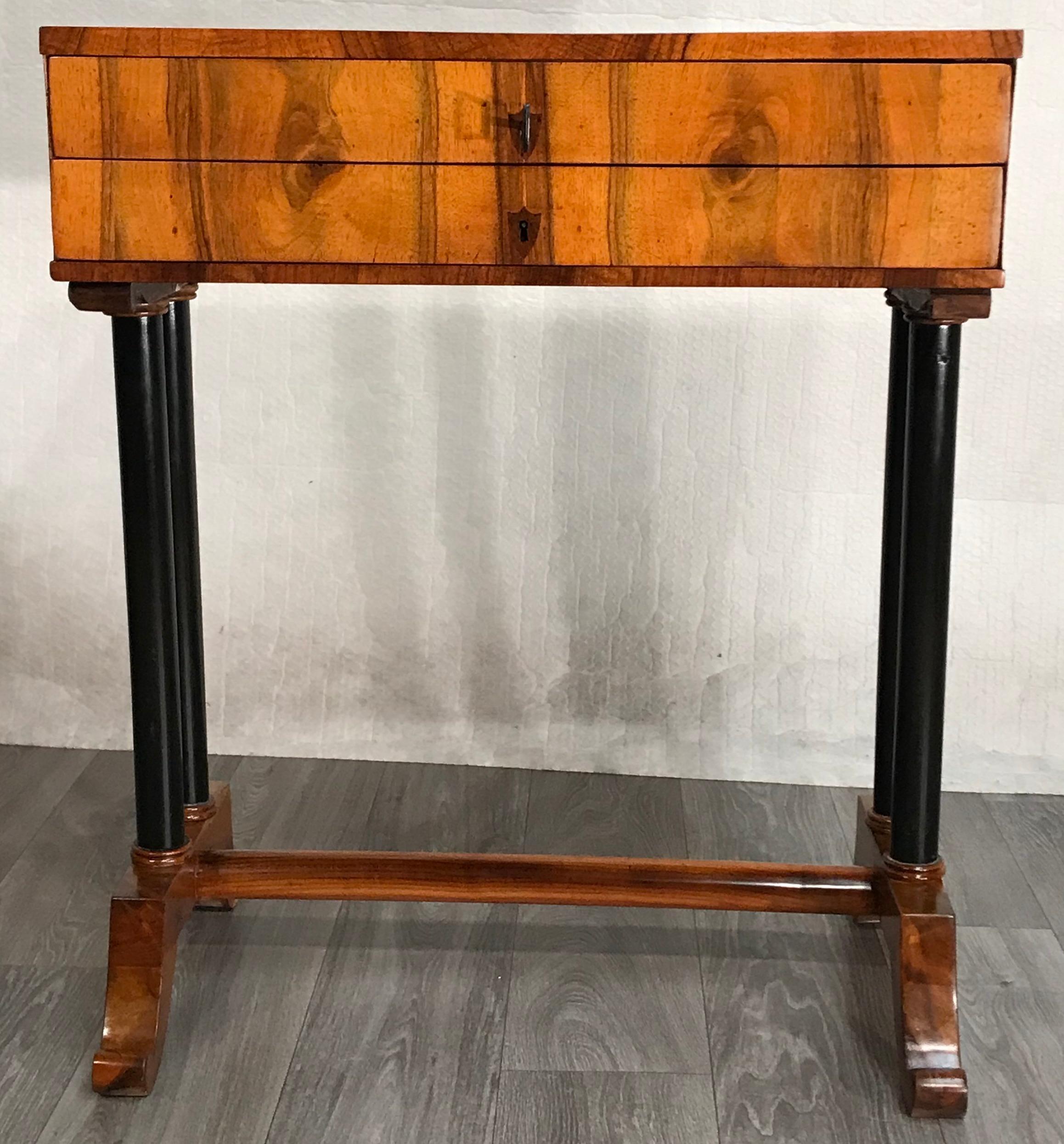 Biedermeier side- or sewing table, South German 1815, walnut veneer. 
This classic unique Biedermeier table has two ebonized columns on each side, which stand on a walnut base connected with a stretcher. The plain rectangular top has two drawers.