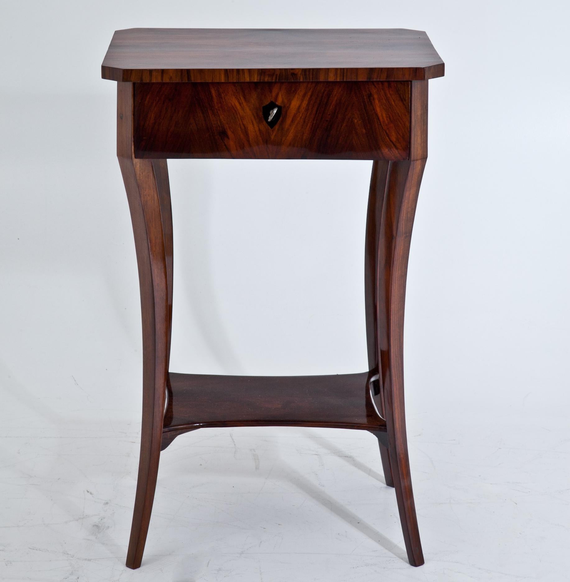 Biedermeier side table standing on slender, slightly curved legs with a concave shelf between them. Above is one drawer with an ebonized escutcheon and slanted corners. Very beautiful walnut veneer. Beautiful hand-polished condition.