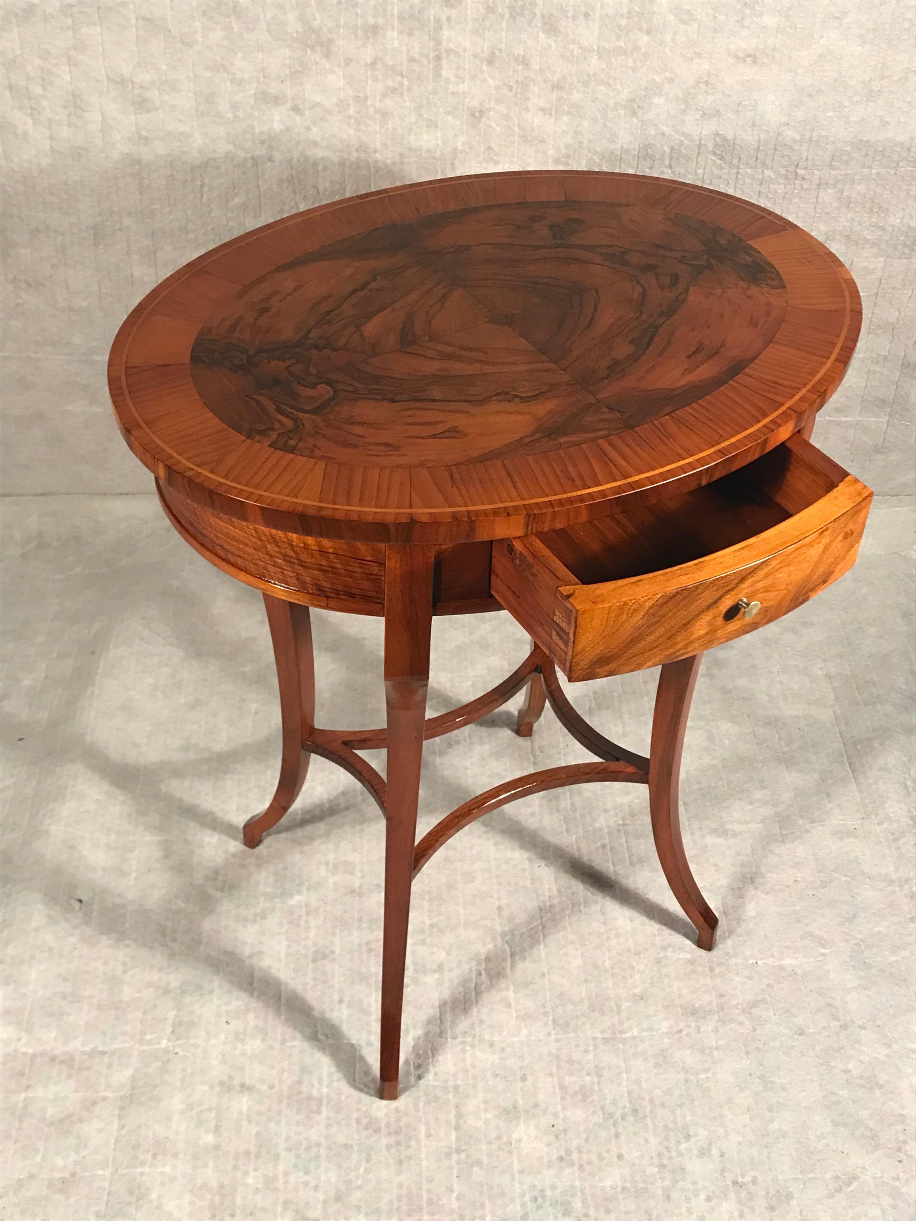 Entdecken Sie den Charme unseres Biedermeier-Beistelltischs im Vintage-Stil mit seinem beeindruckenden Walnussfurnier. Dieser elegante, ovale Tisch mit zentraler Schublade stammt aus Süddeutschland und wurde 1820 gefertigt. Er ist ein zeitloses