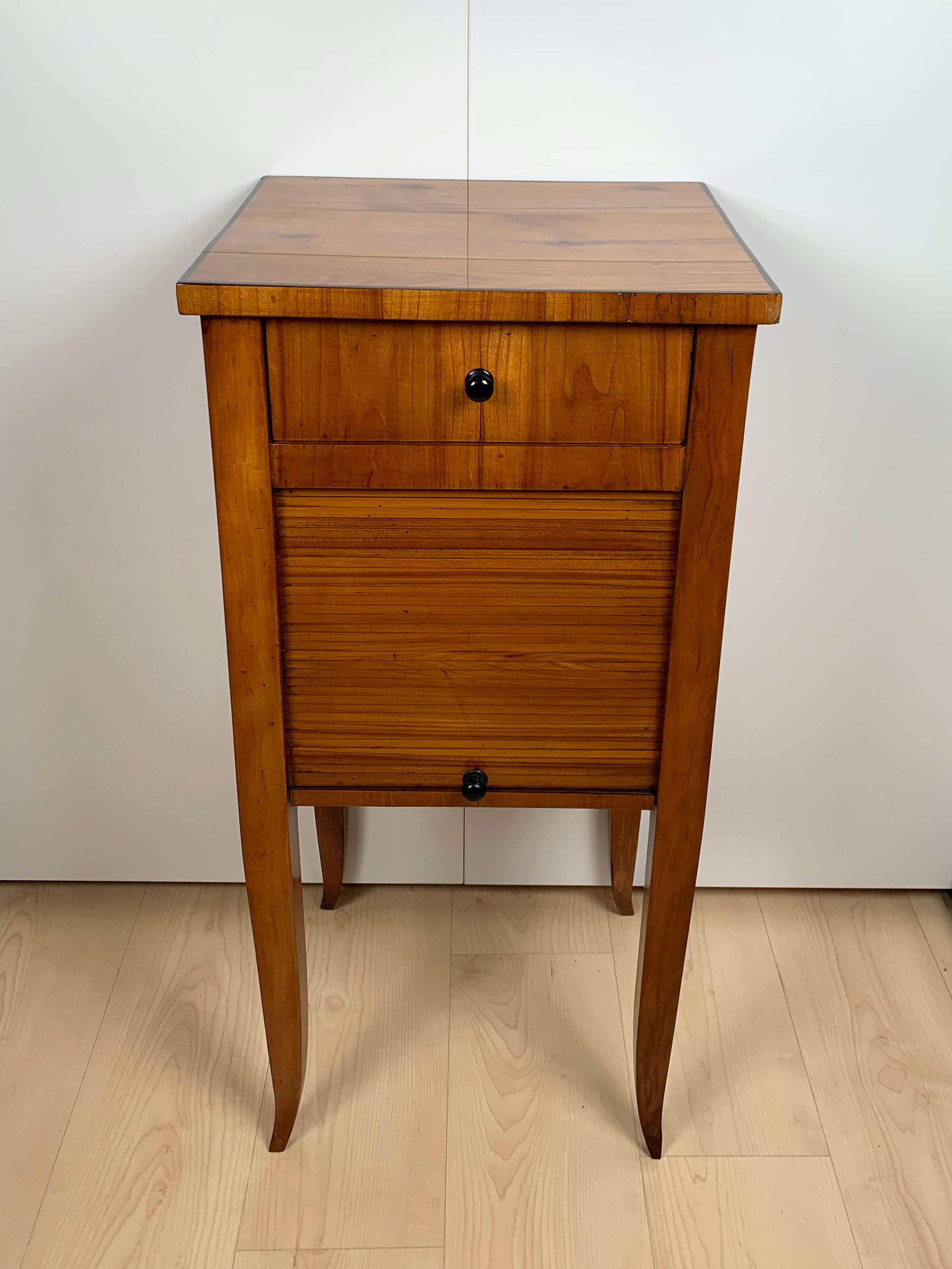 Wonderful, restored Biedermeier small furniture / pillar cabinet / Nightstand in bright Cherry Veneer from South Germany around 1820.

One drawer and one roller shutter at the front. Four sides and top in cherry veneer on softwood. Ebony trim