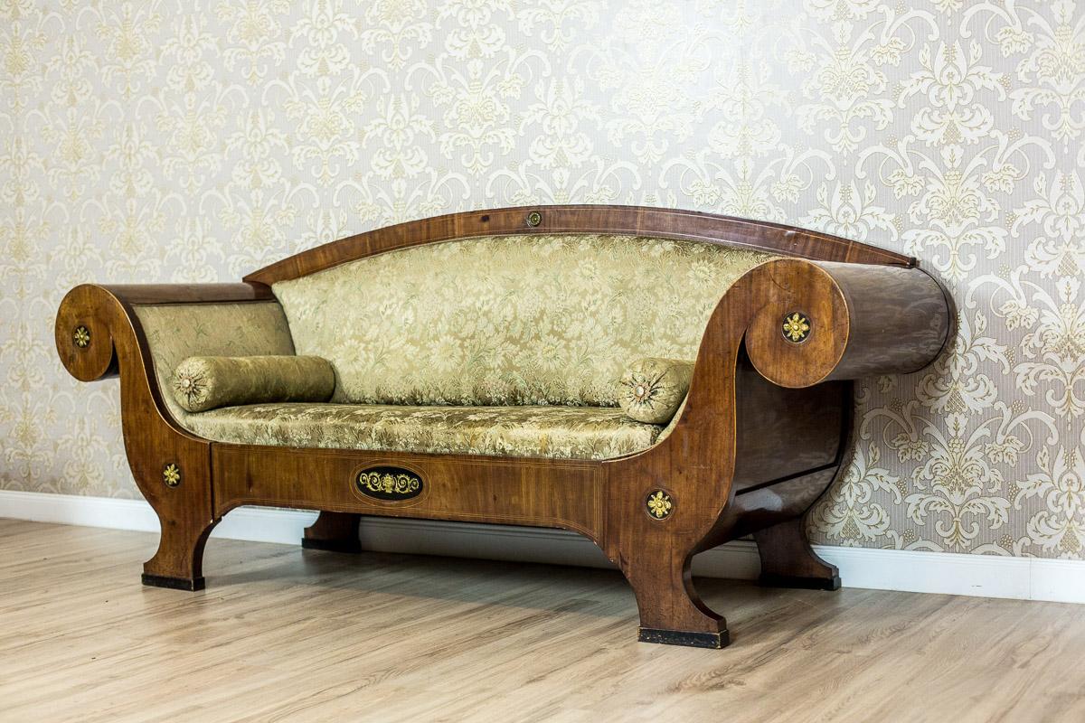 We present you this massive sofa, typical for the Biedermeier style, with a softly upholstered seat and backrest. This article of furniture has characteristically rolled outwards, volute armrests, and a slightly semicircular backrest. The wooden