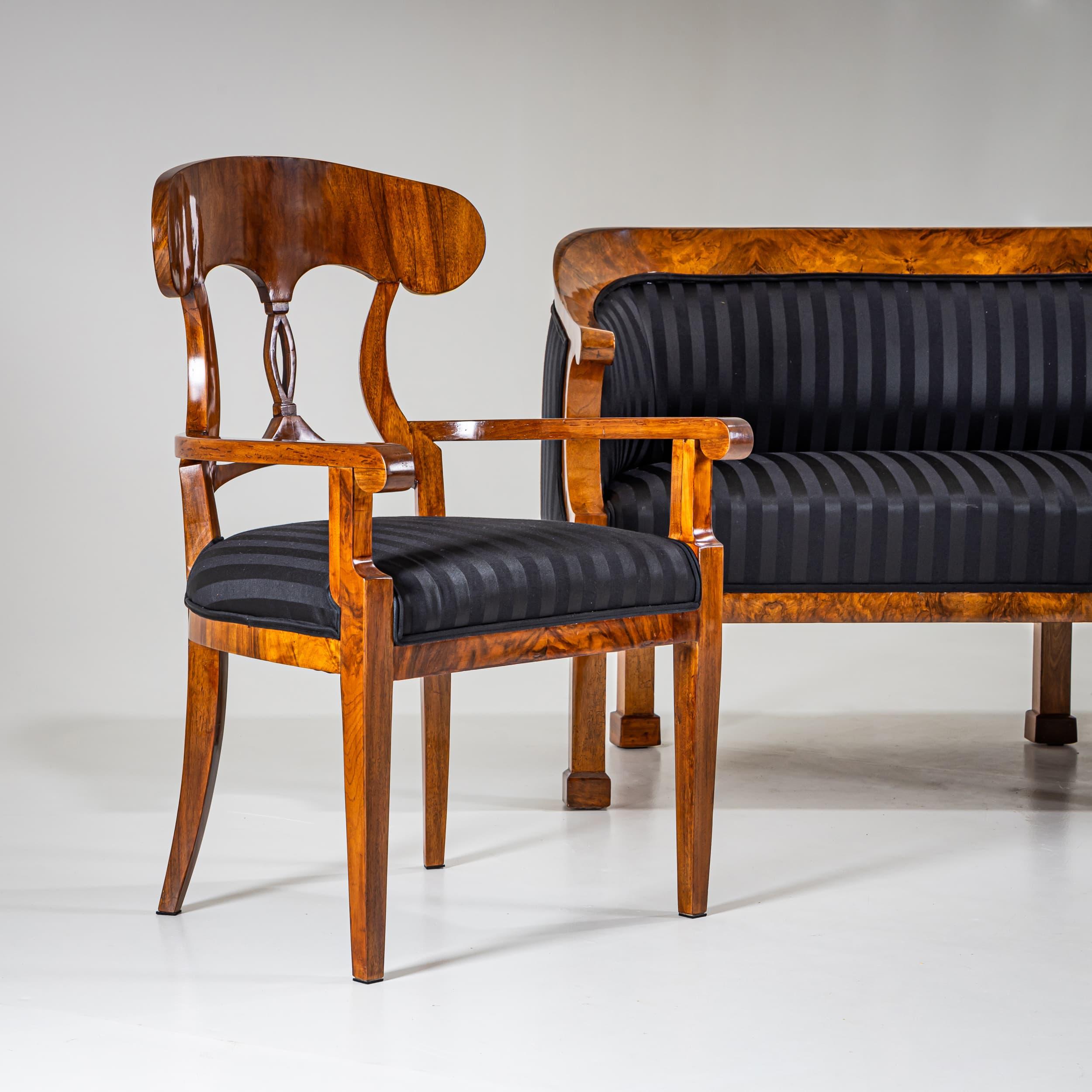 Large sofa raised on six block feet with a rounded backrest terminating in stylized volutes at the armrests. Veneered in walnut and hand-polished. The seat has been newly upholstered and covered with a black striped fabric.